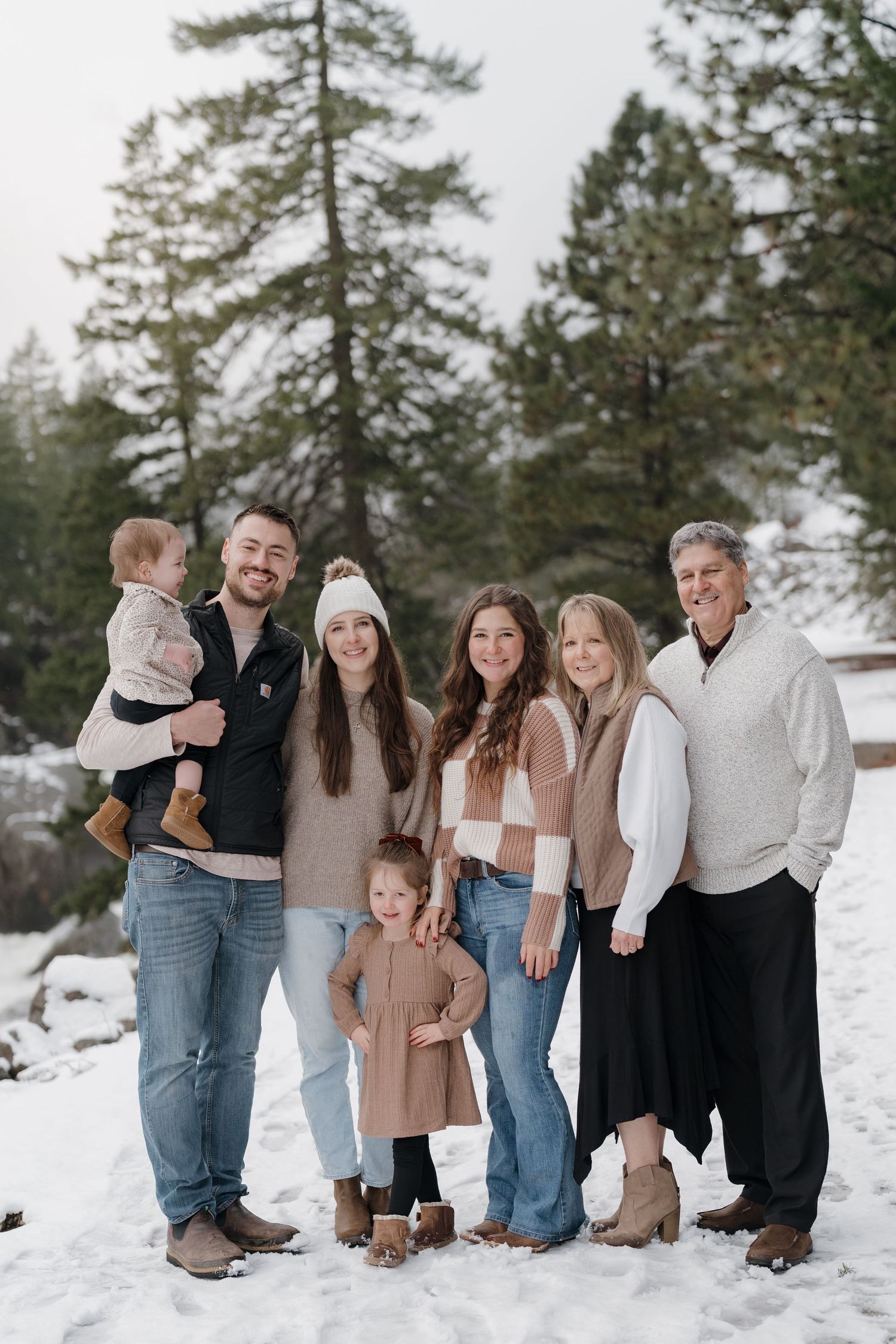 Multi-generational family posing together in snowy winter landscape with tall pine trees in background.
