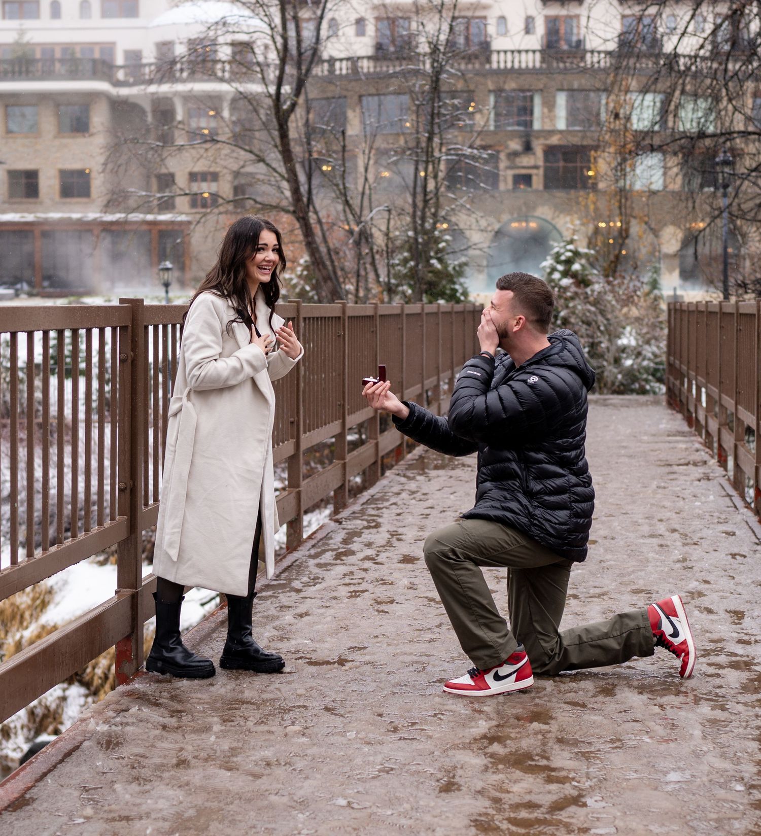 A couple shares a romantic proposal moment on a wooden bridge during winter with snow-covered surroundings. Leavenworth, WA