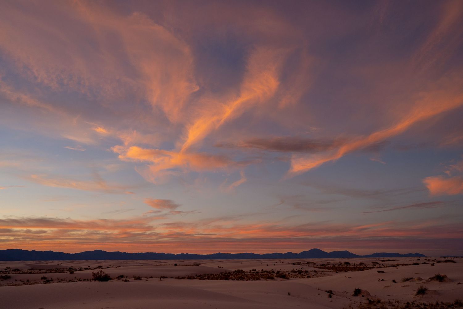 Dramatic pink and orange clouds sweep across the sky above White Sands National Park at sunset in New Mexico.