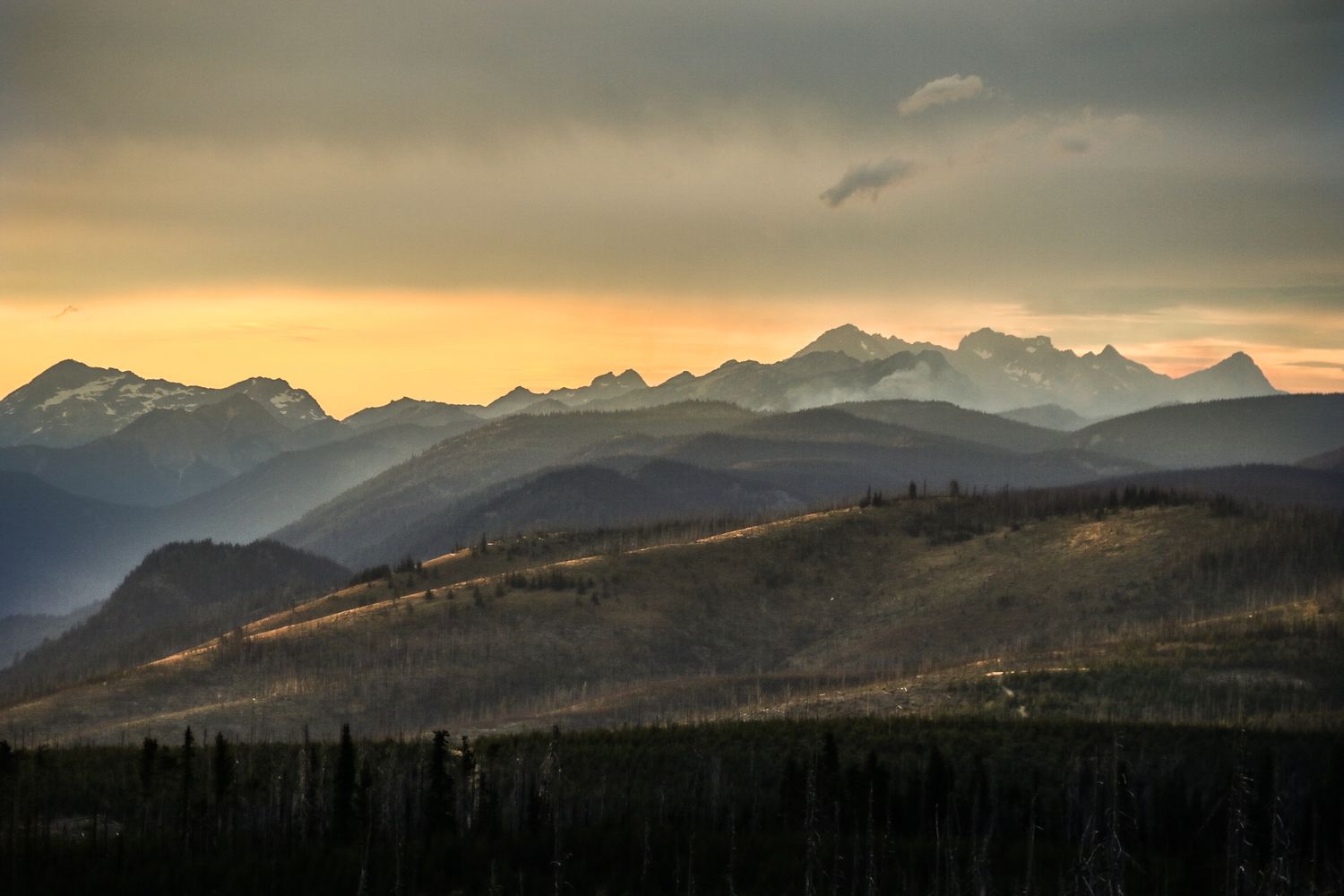 Golden sunset light illuminates mountain peaks against a dramatic cloudy sky.