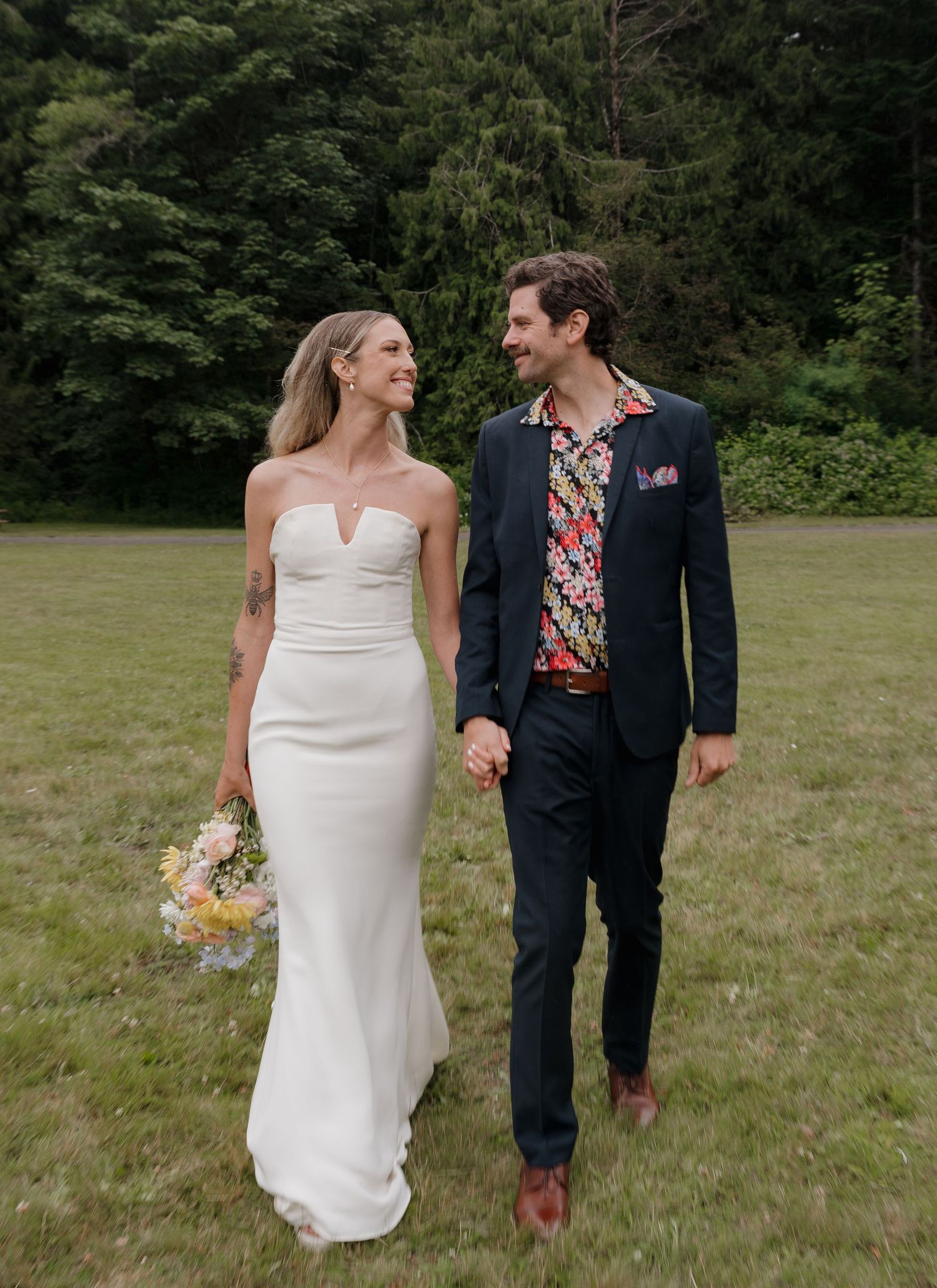 A couple shares a romantic moment while walking together on a grassy field during their wedding day.