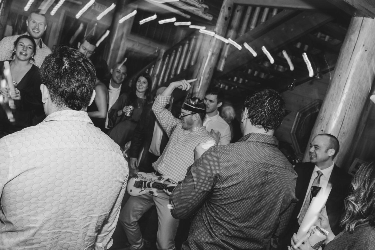 Black and white photo of wedding guests dancing and celebrating at an indoor reception.