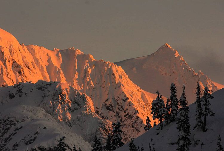 Snow-capped mountain peaks glowing orange in alpenglow during sunset.