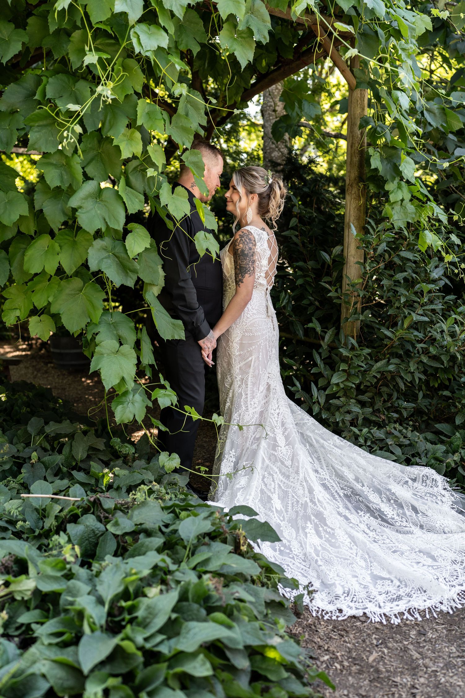 Elegant wedding couple poses among ivy-covered walls with trailing lace gown.