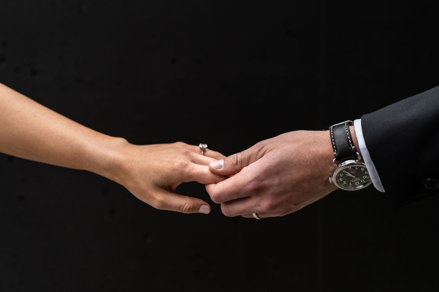 Close-up of hands exchanging wedding rings against a dark background.