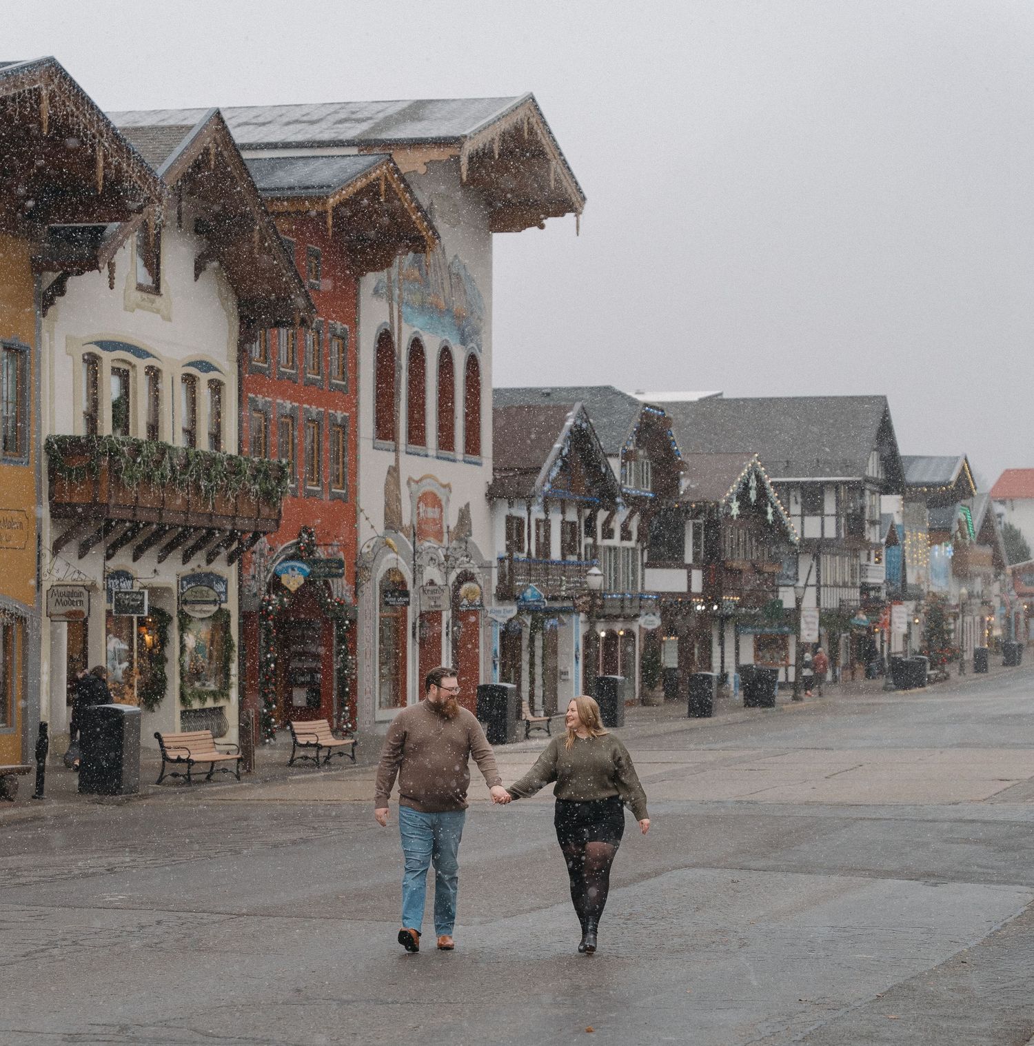 Couple holding hands walking through snowy Bavarian-style village street in Leavenworth, Washington.