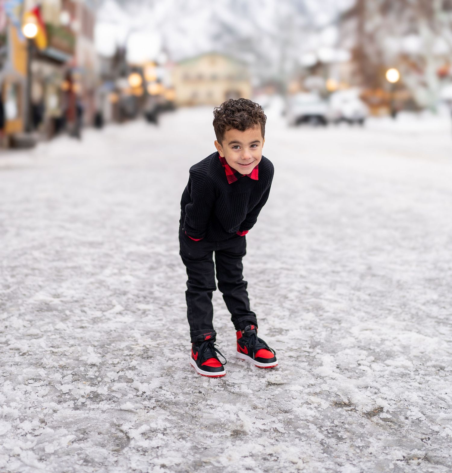A child wearing black clothing and red shoes plays in the snow on a winter day. Leavenworth, WA