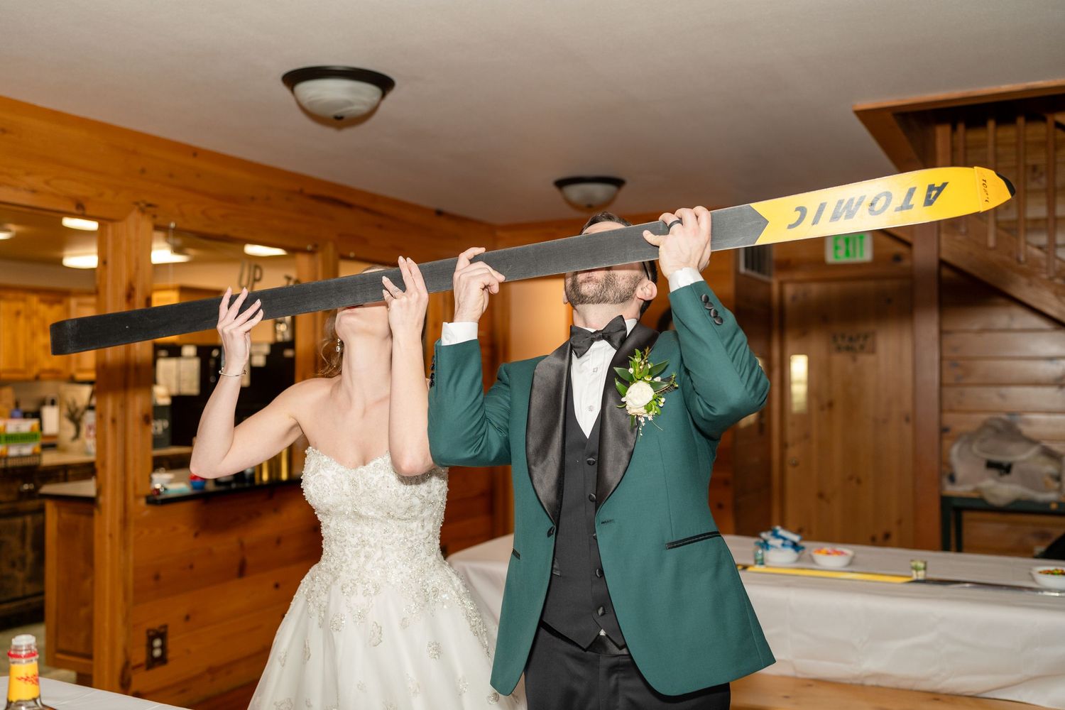 Wedding couple celebrating with arms raised in a wood-paneled reception venue.