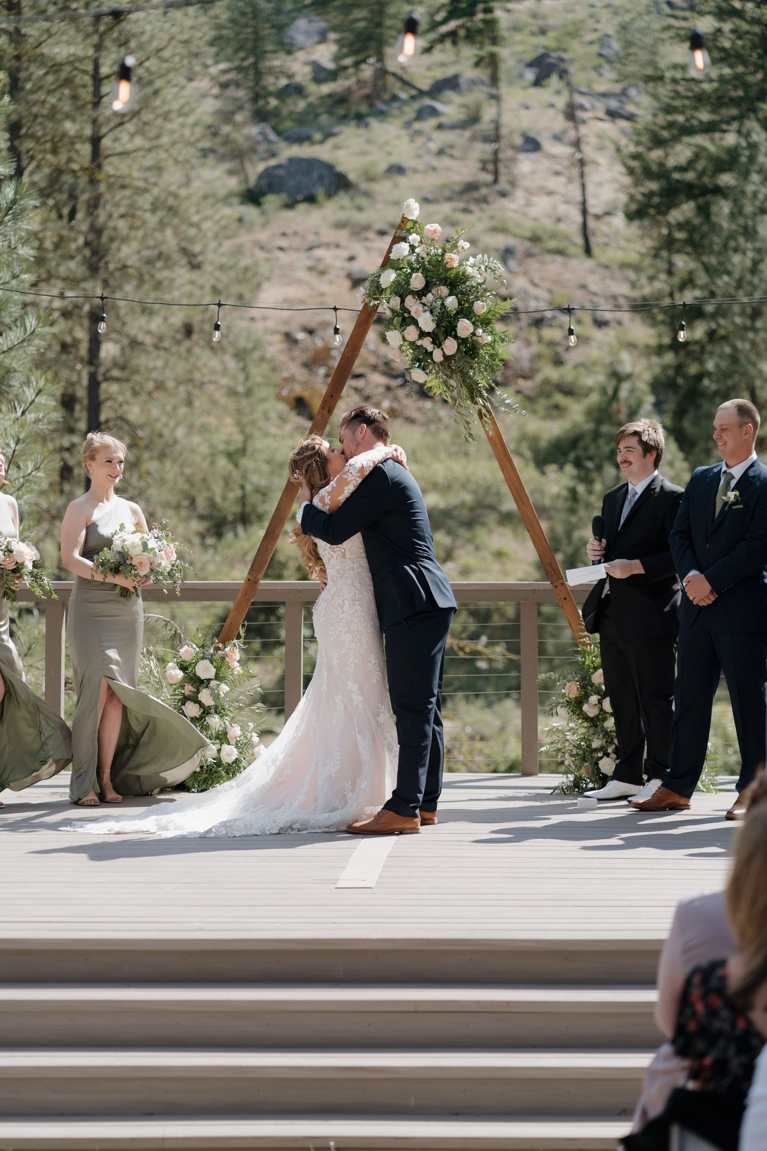 A couple shares a romantic dip during their outdoor mountain wedding ceremony on a wooden deck.