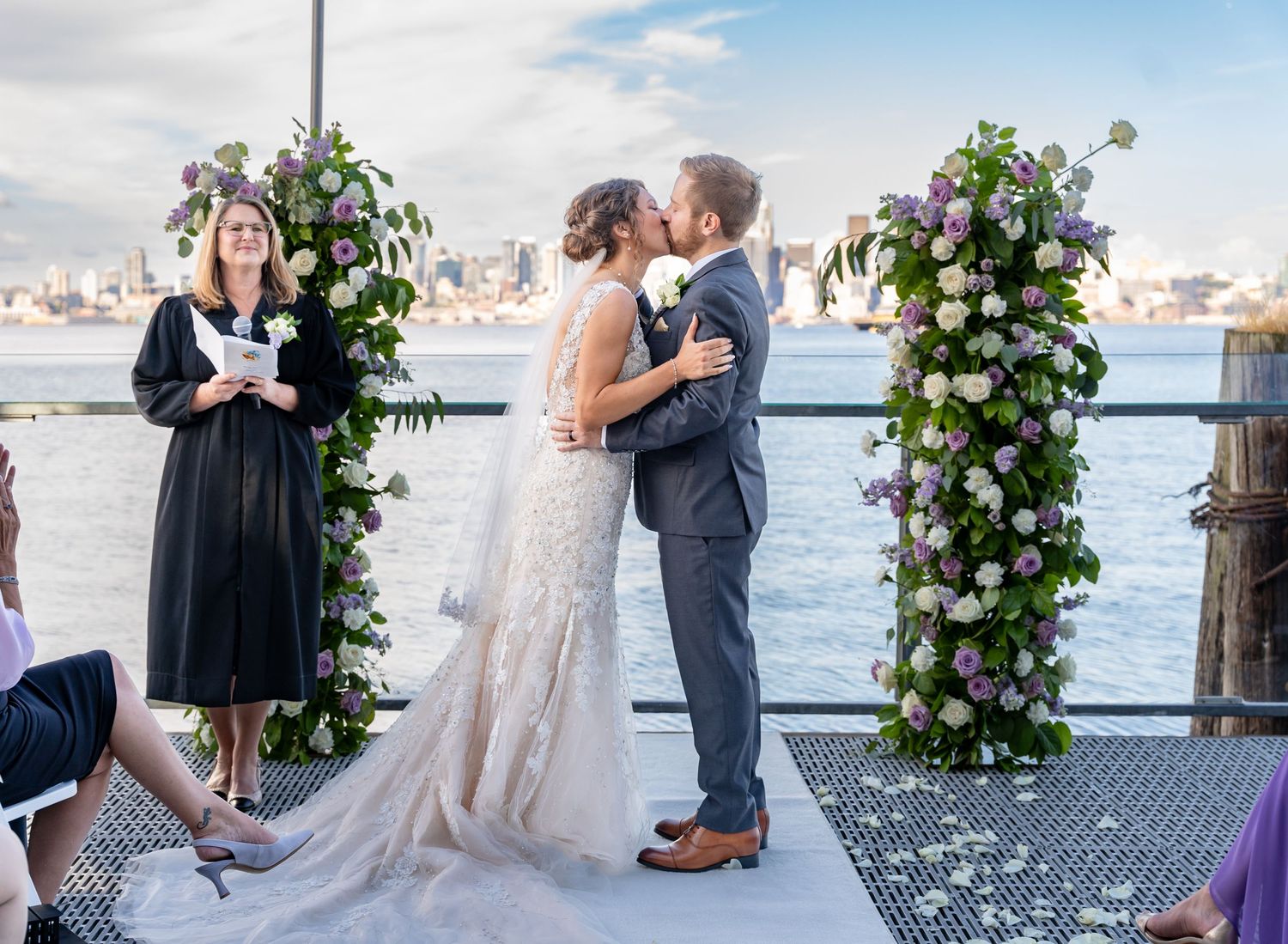 Wedding ceremony under floral arches on waterfront dock with city skyline backdrop.