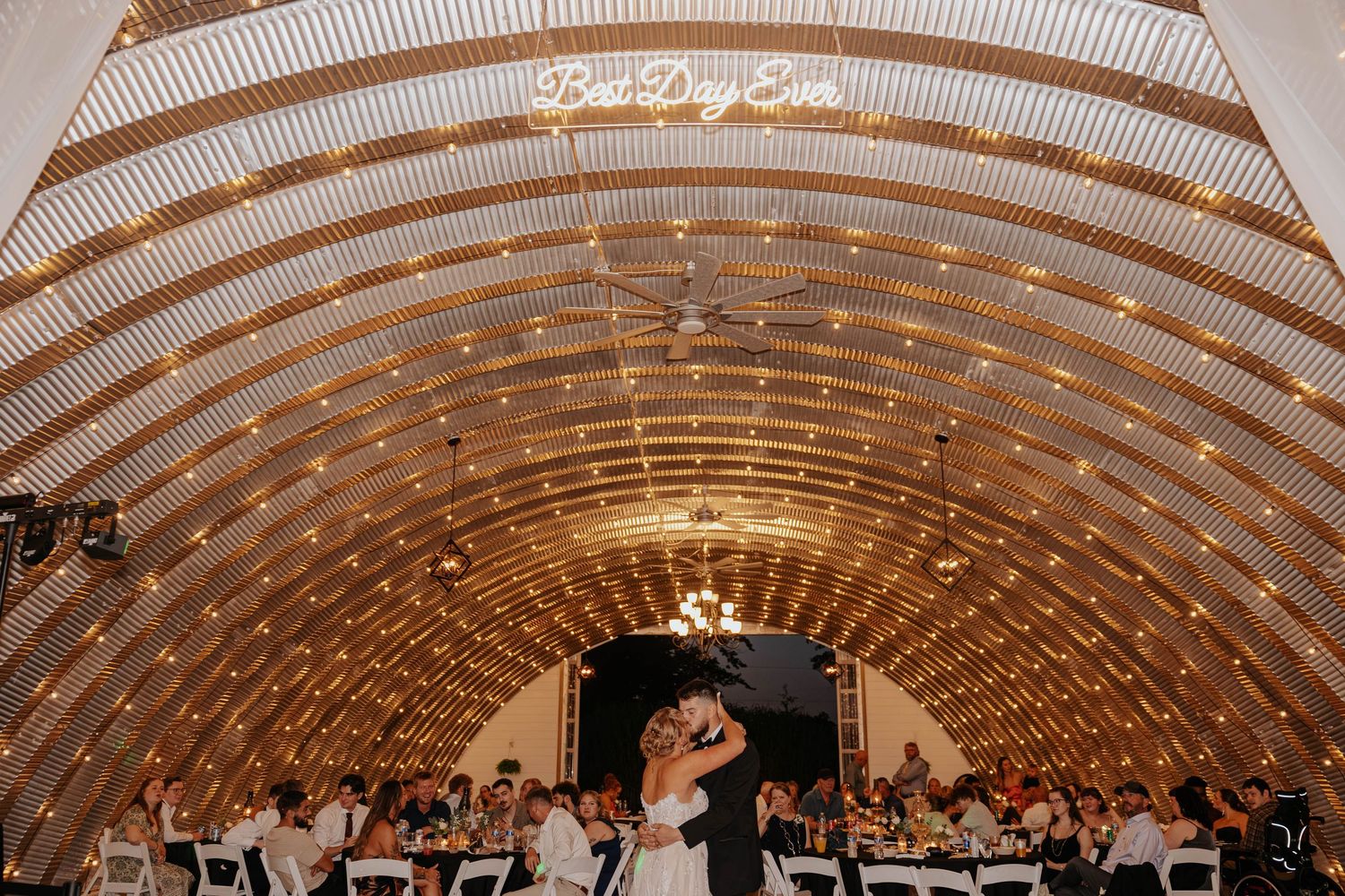 Bride and groom share a romantic moment beneath the glowing lights of the arched barn at Res-Les Farms in Michigan.