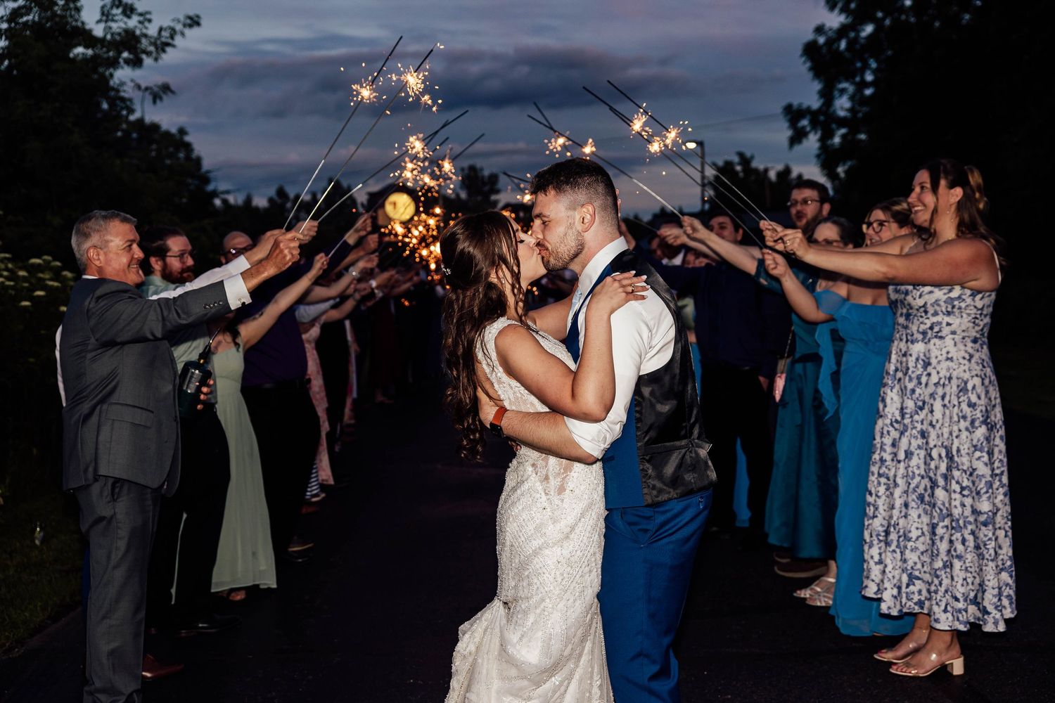 Bride and groom kissing beneath glowing sparklers held by wedding guests during an evening wedding celebration in Fenton, Michigan.