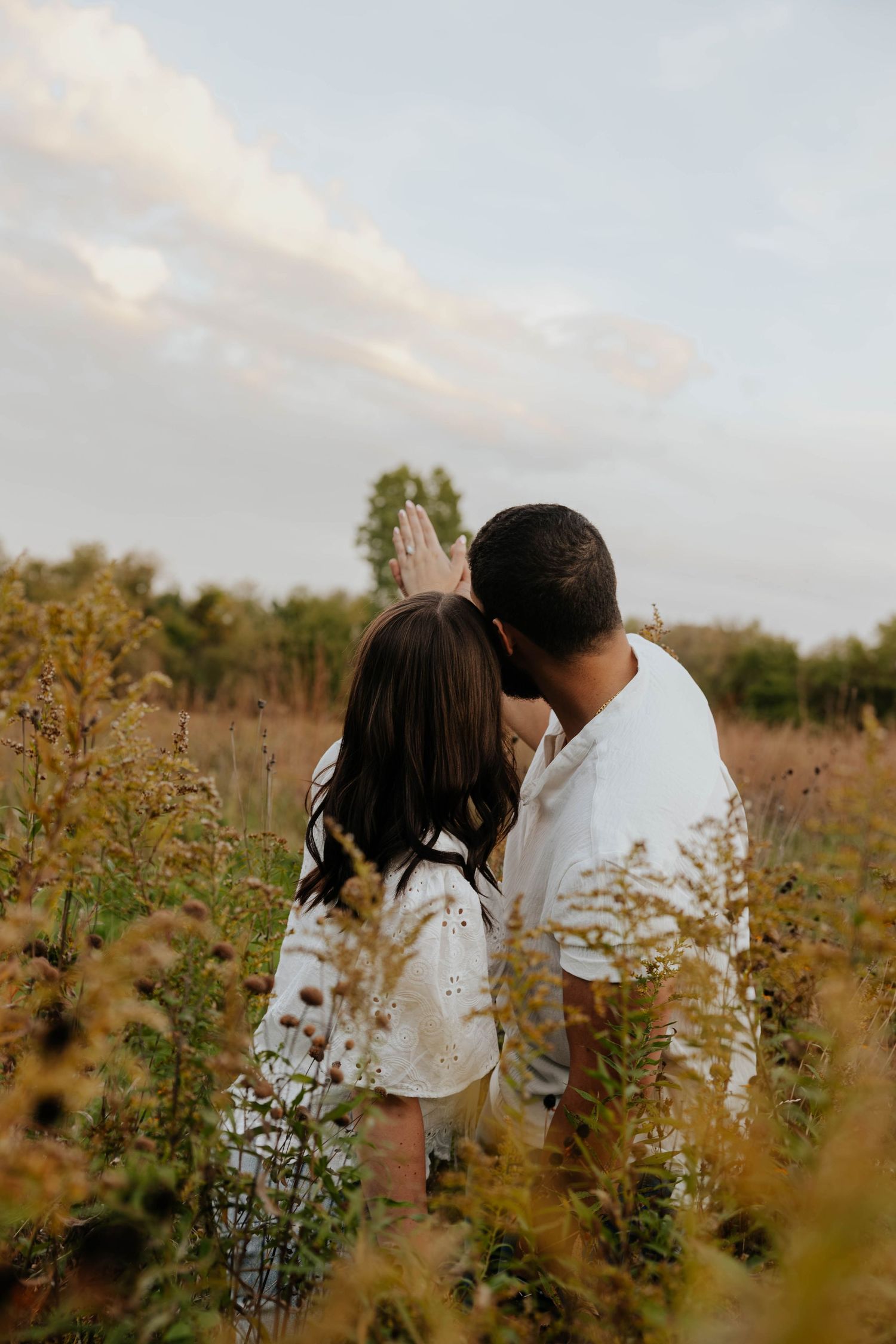 Romantic engagement photo of a couple embracing among wildflowers at sunset in Caledonia, Michigan.