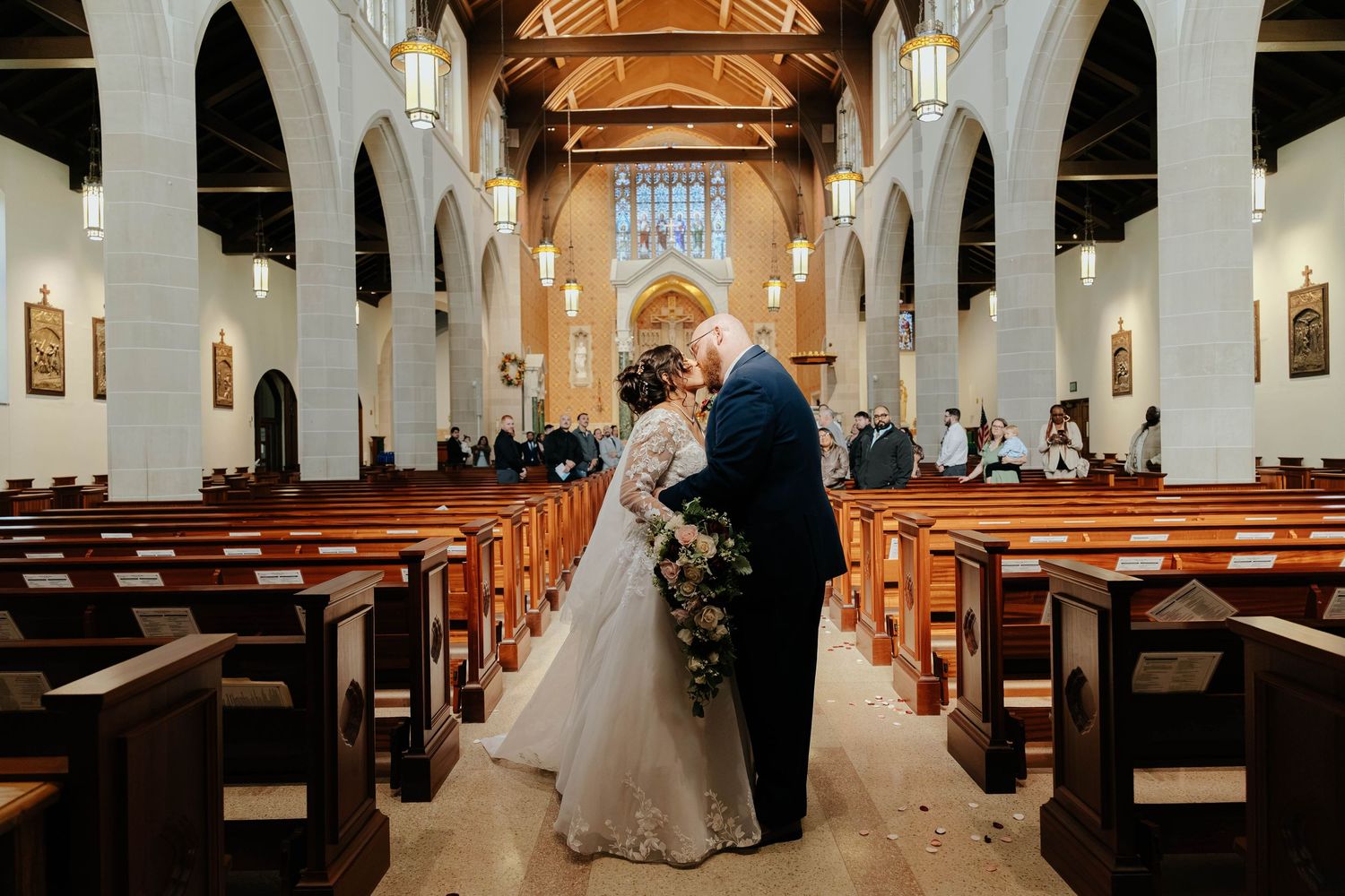 Bride and groom embrace in the center aisle of a beautiful Catholic church following their wedding ceremony in Kalamazoo, Michigan.