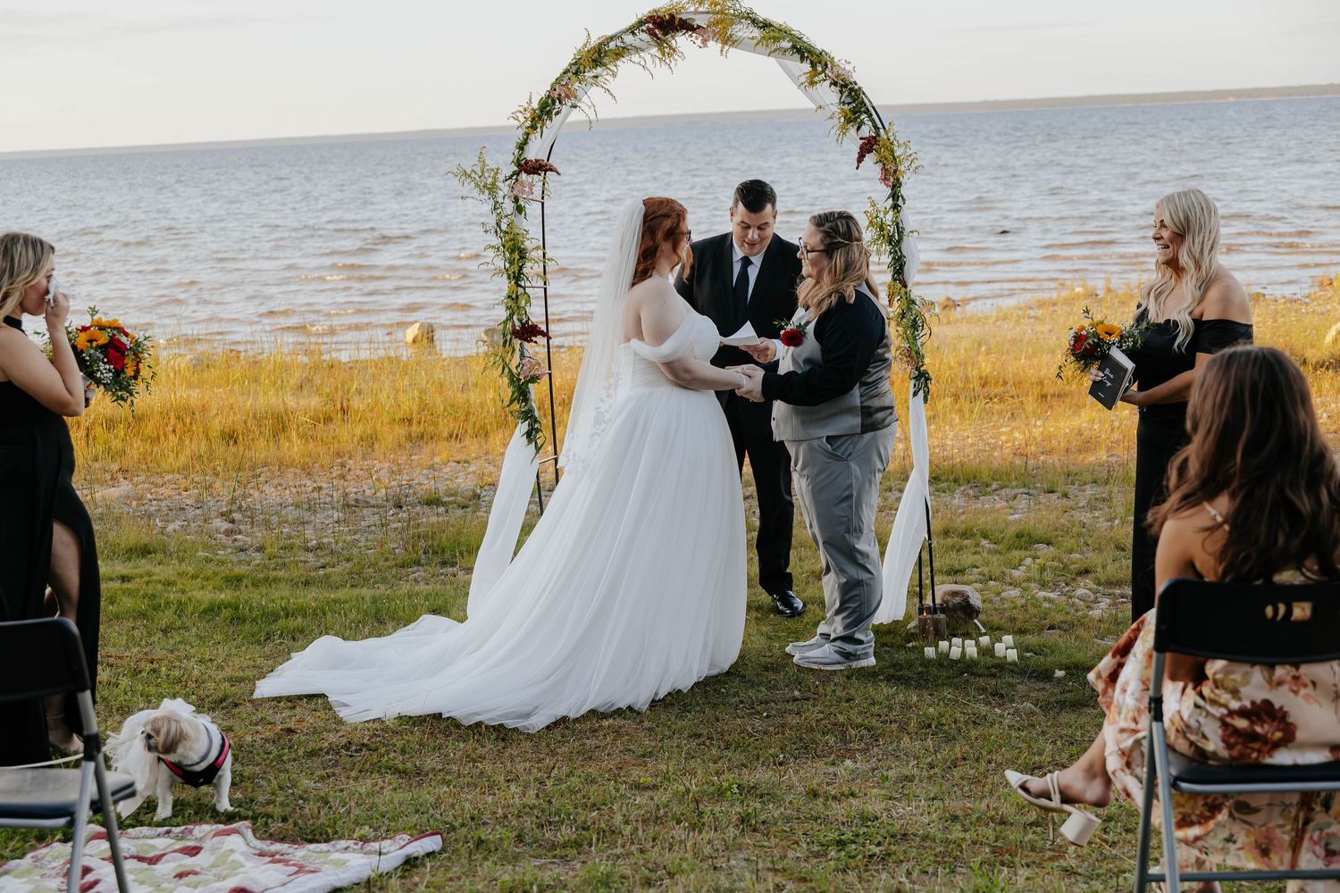 Intimate Northern Michigan lakeside elopement ceremony with a floral wedding arch, scenic water views, and loved ones gathered nearby.