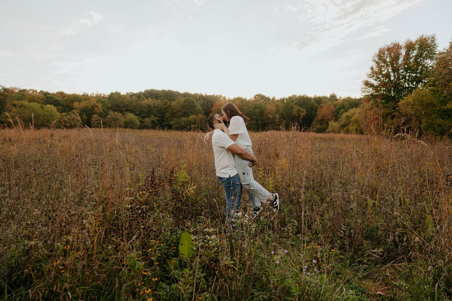 Romantic outdoor engagement photos of a couple embracing in a tall grassy field surrounded by autumn colors in Caledonia, Michigan.