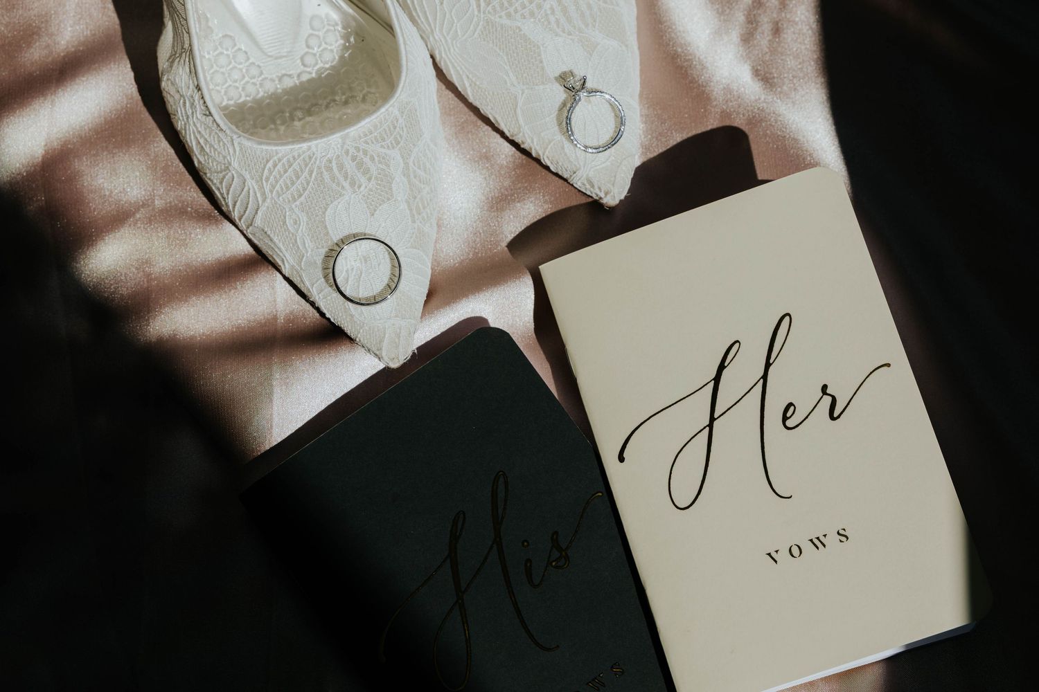 Close-up wedding detail photo featuring personalized His and Hers vow books and wedding accessories arranged together.