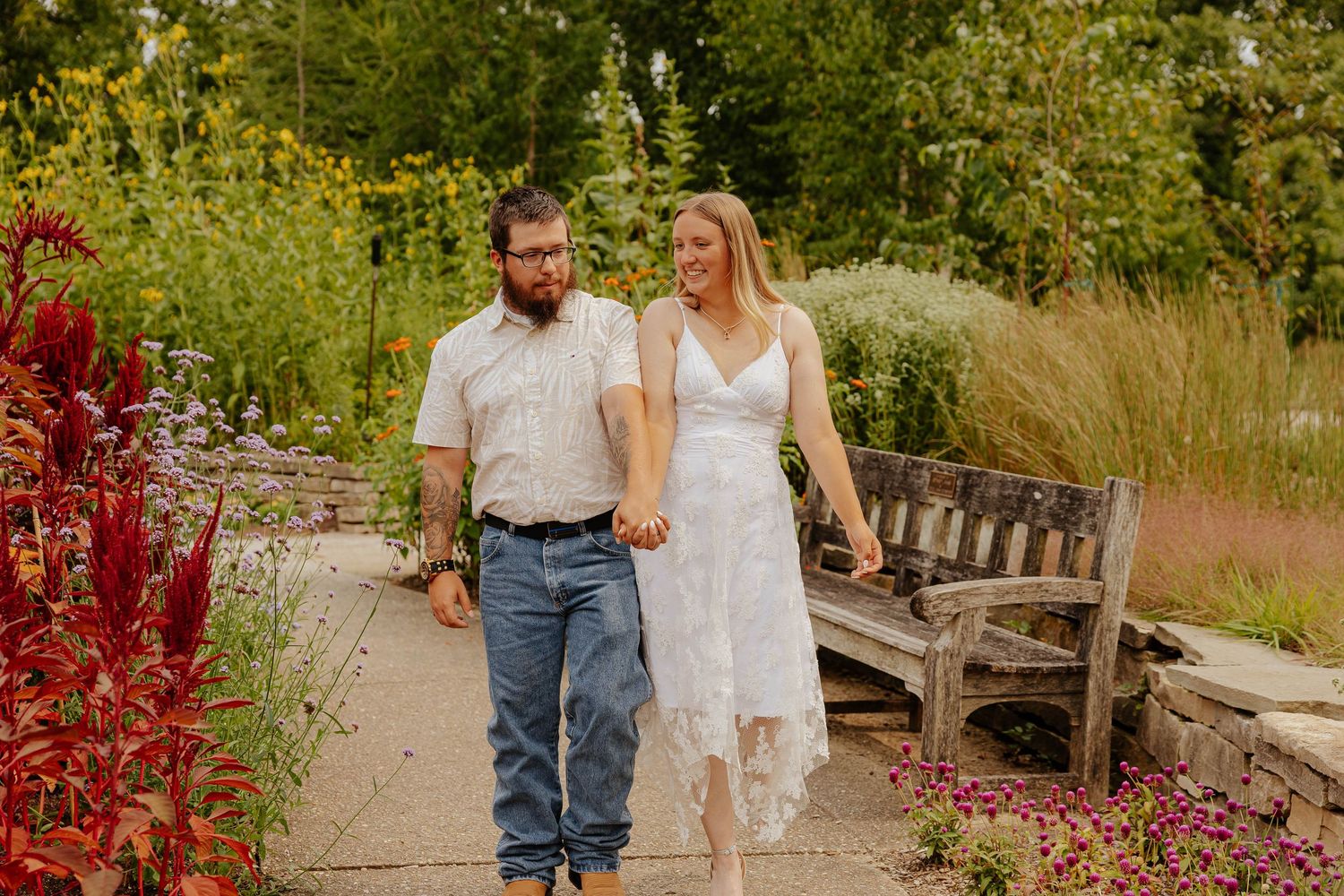 Couple walking hand in hand through a colorful botanical garden during a romantic outdoor engagement photography session in Michigan.