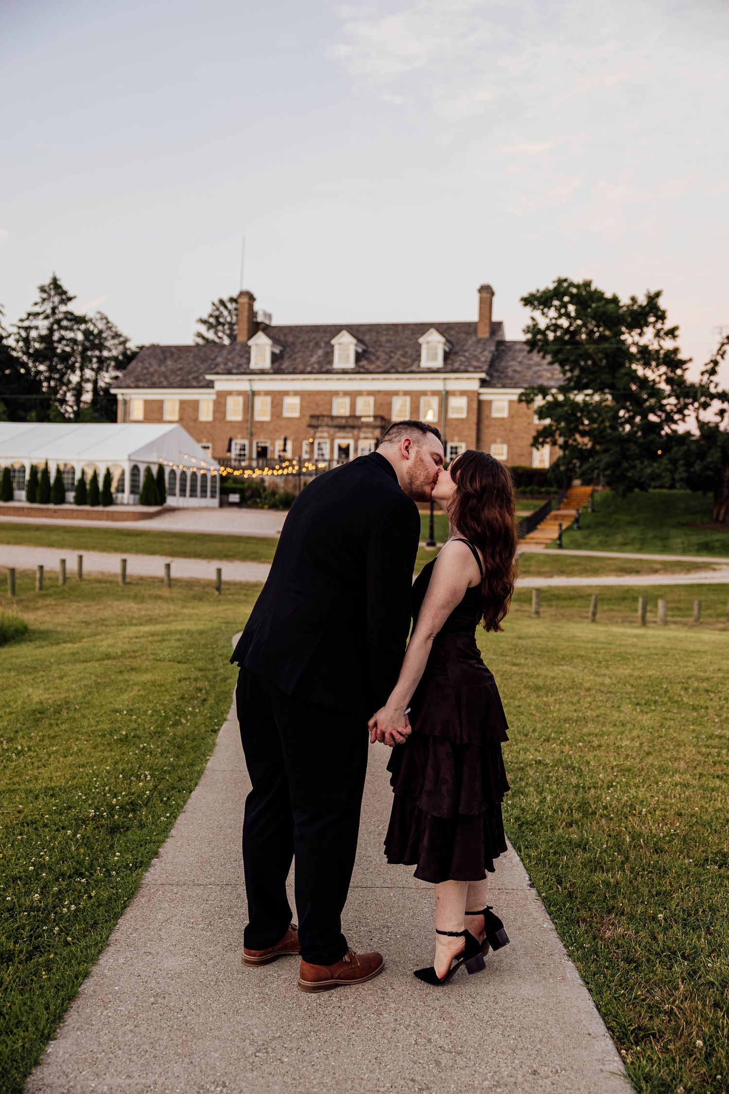Romantic engagement photos of a couple kissing on a garden pathway with historic Felt Estate in the background in Saugatuck, Michigan.