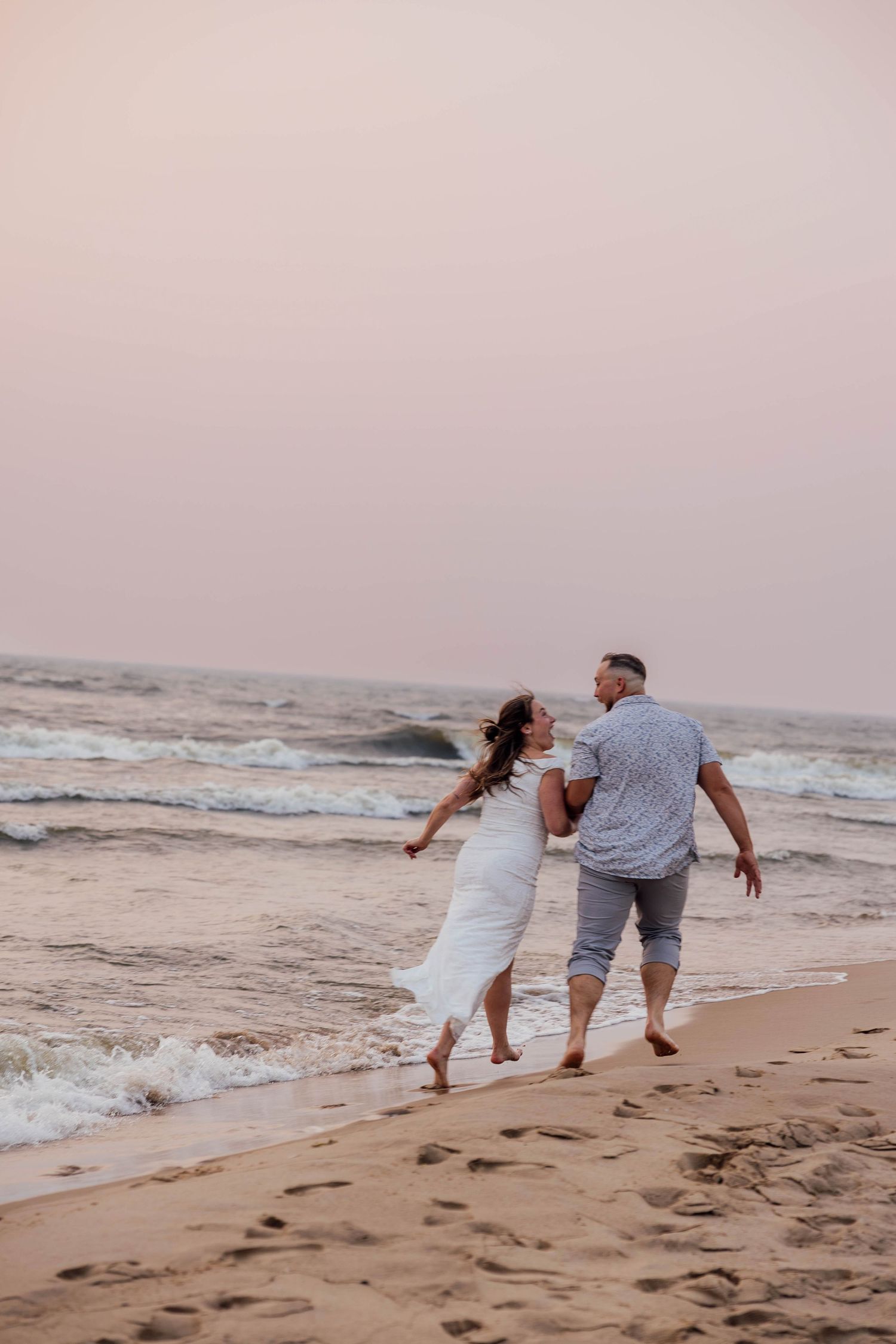 Romantic beach engagement photos of a couple running hand in hand along the Lake Michigan shoreline at sunset near Saugatuck.