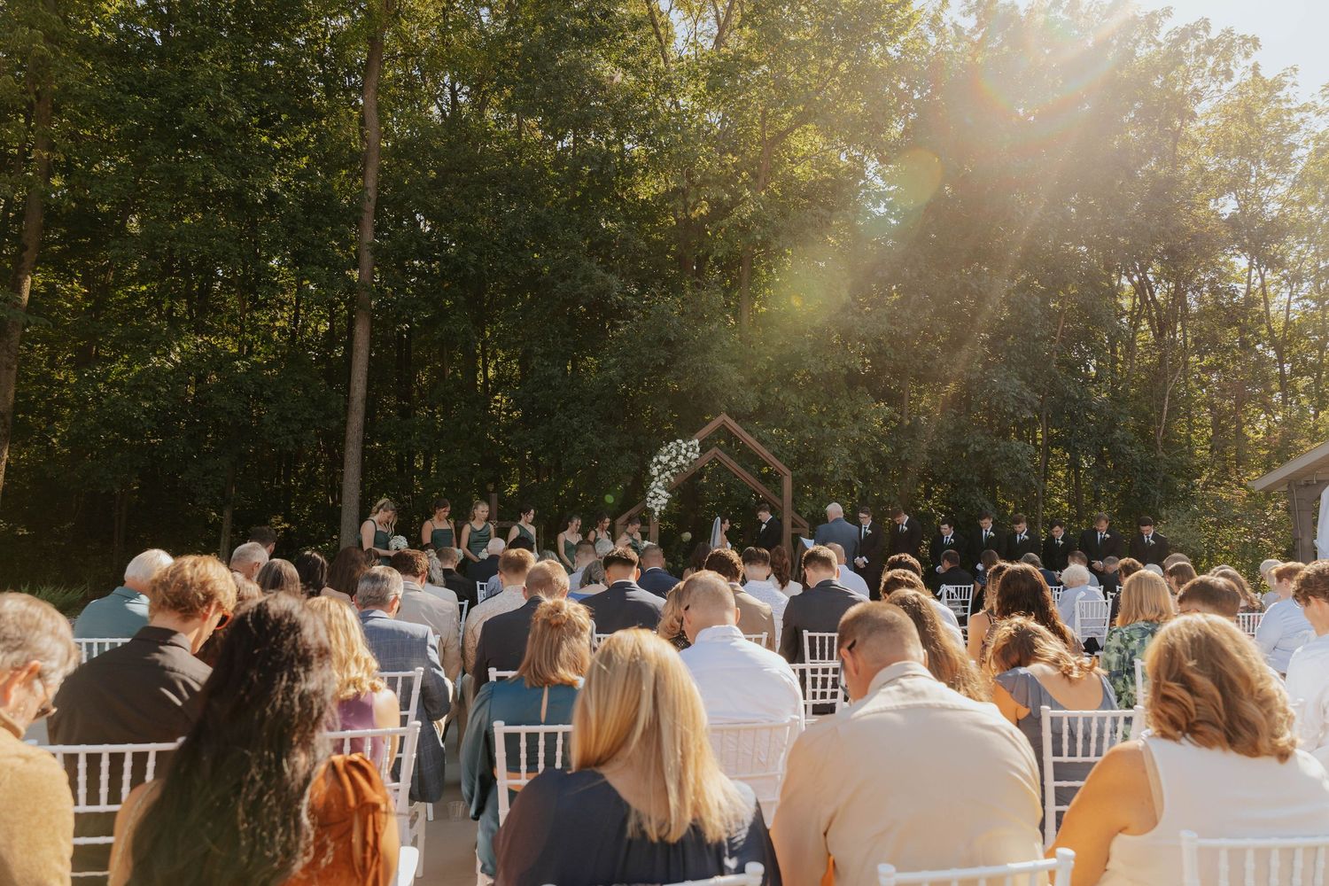 Romantic outdoor wedding ceremony at Hidden Oak Manor in Indiana, with guests seated beneath the trees in golden sunlight.