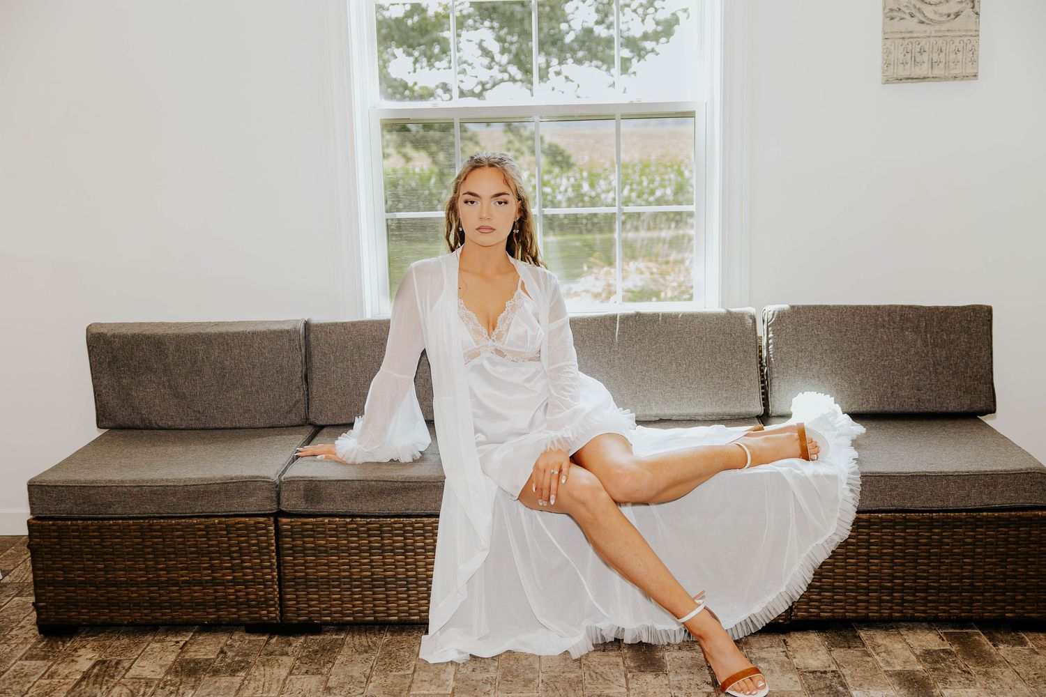 Bride relaxes on a couch in her white bridal robe before getting dressed for her wedding at The Gather in Allegan, Michigan.