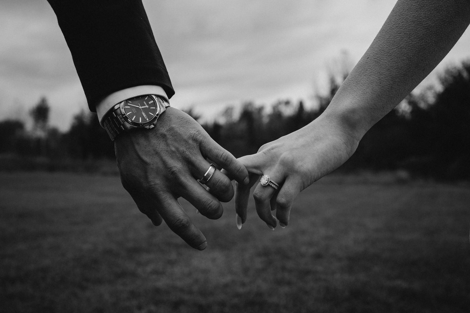 Black-and-white close-up of a bride and groom gently holding hands, showing their wedding rings during an intimate wedding moment.