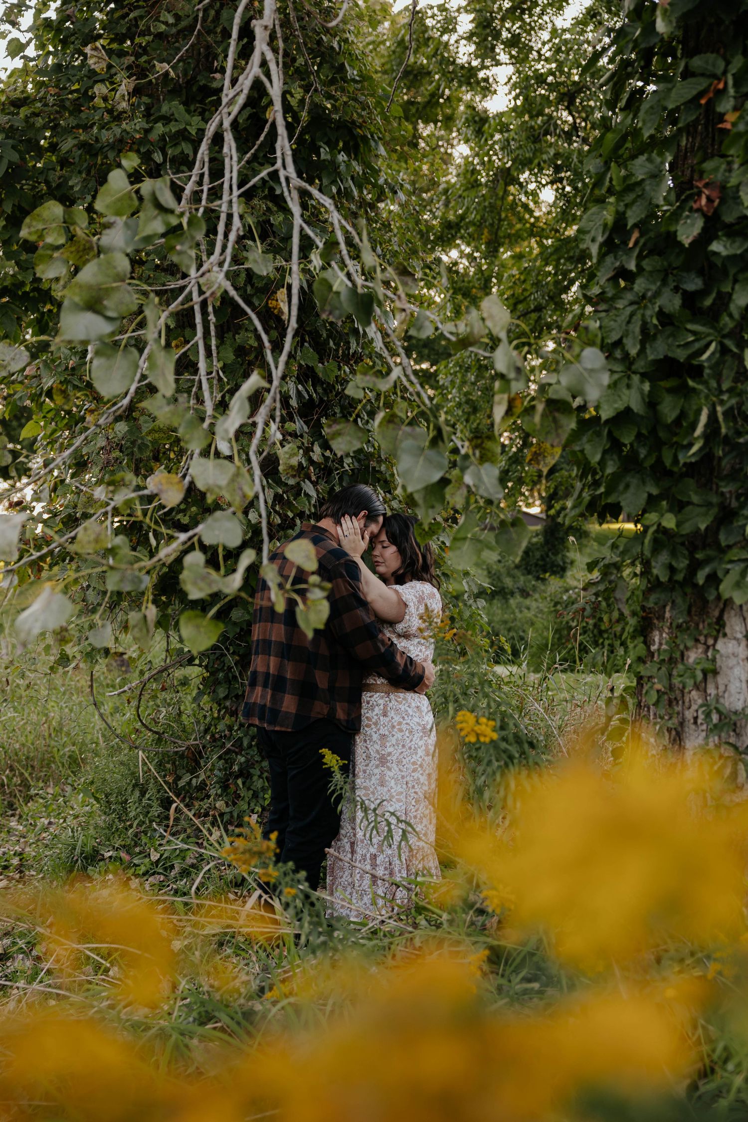 Outdoor engagement portrait of a couple embracing among yellow wildflowers and lush greenery near Lake Odessa, Michigan.