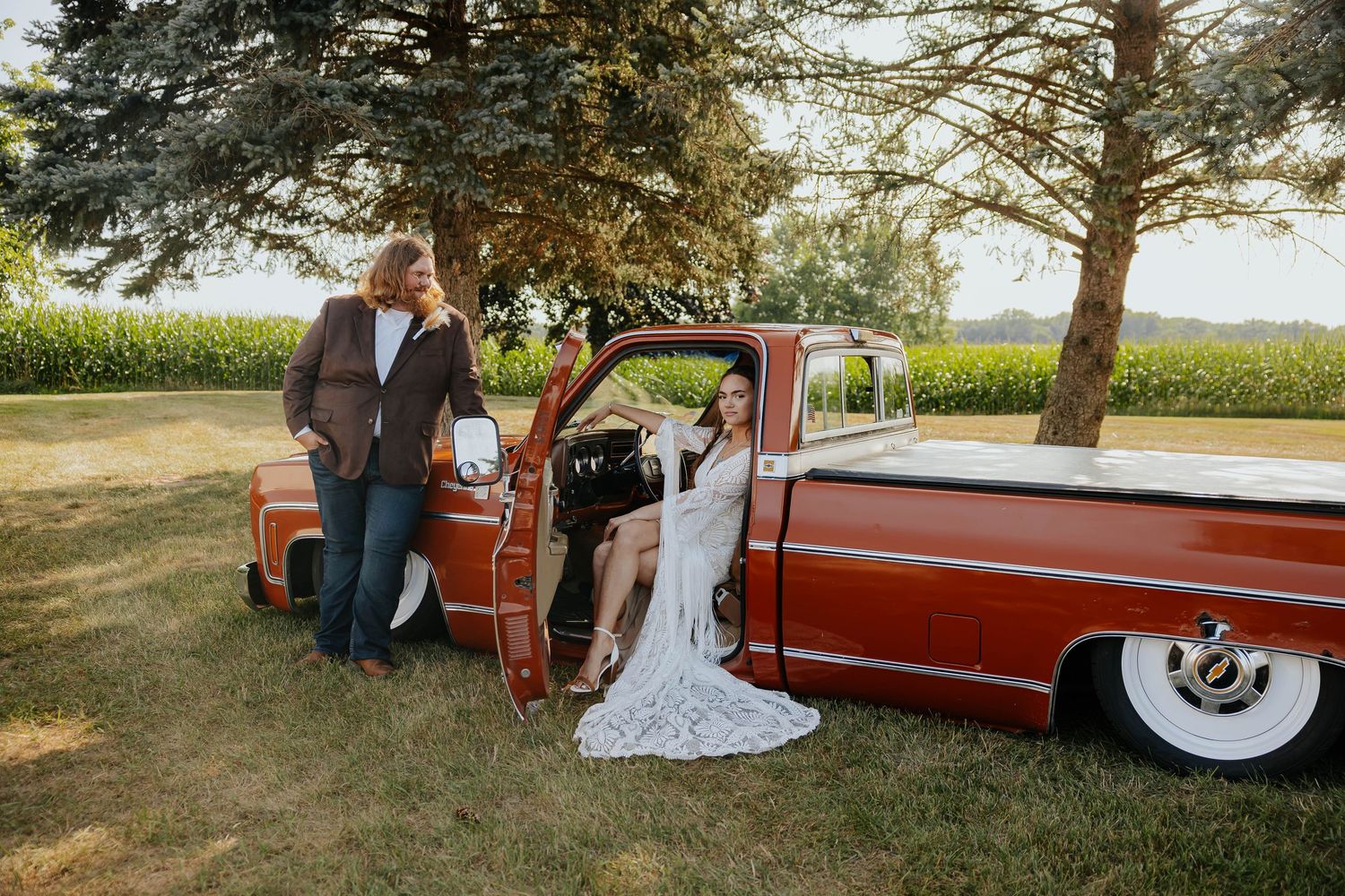 Rustic wedding photo of a bride and groom posing beside a vintage red pickup truck at The Gathering in Allegan, Michigan.