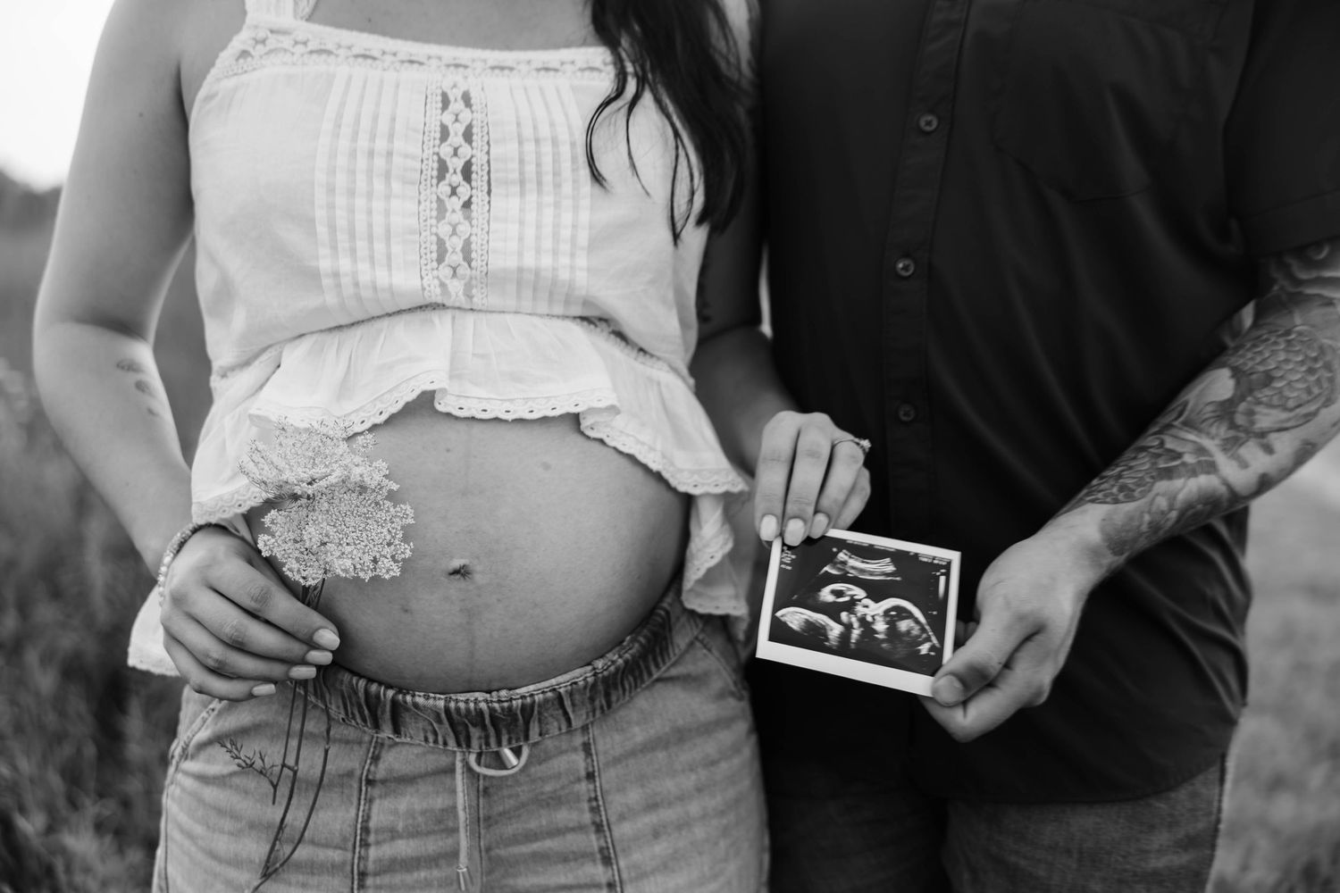 Black-and-white maternity portrait of expecting parents holding an ultrasound photo and cradling the baby bump.
