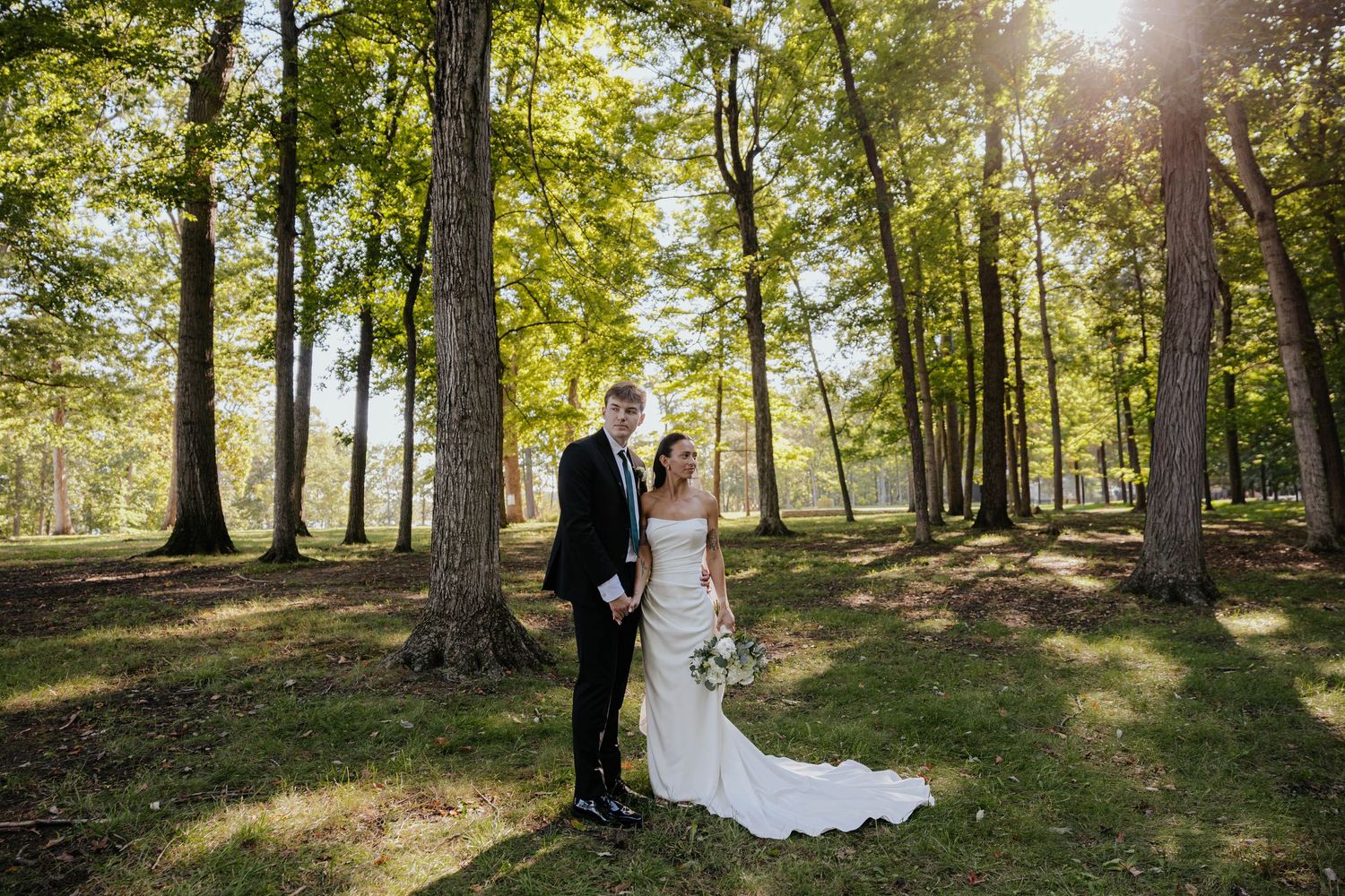 Bride and groom stand together in a sunlit wooded setting for romantic wedding portraits at Hidden Oak Manor in Indiana.