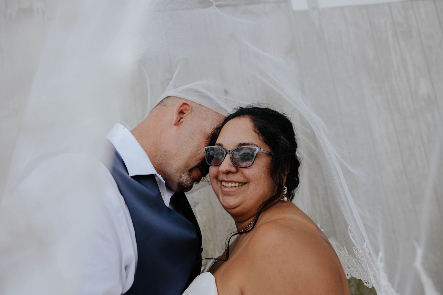 Bride and groom share a romantic close-up portrait beneath her flowing veil during their wedding in Sparta, Michigan.