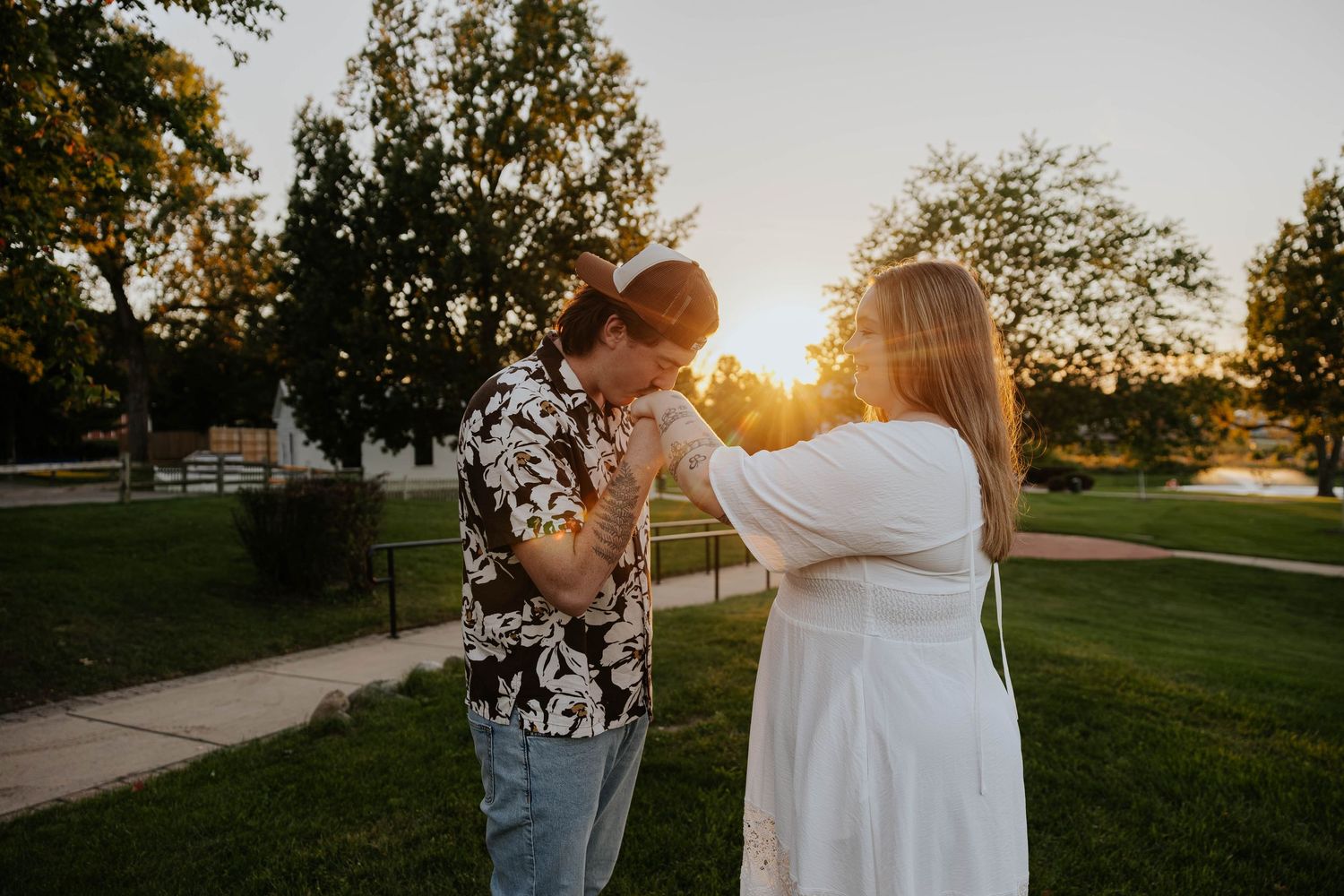 Romantic engagement photo of a couple holding hands and smiling in a grassy park at sunset in Portage, Michigan.