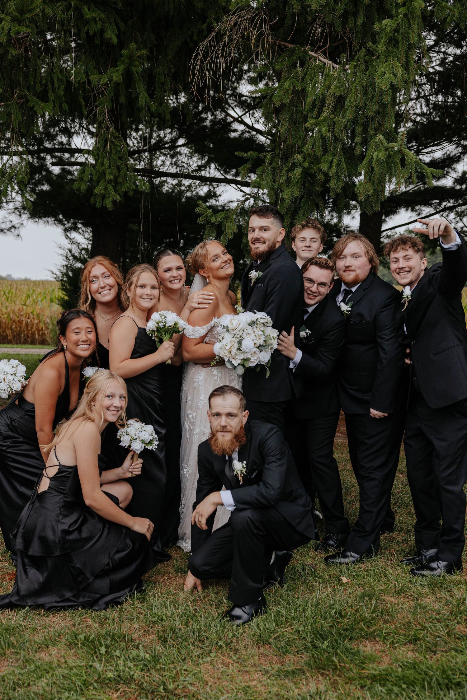 Bride, groom, and wedding party posing together outdoors in coordinated black formal attire during a Michigan wedding.