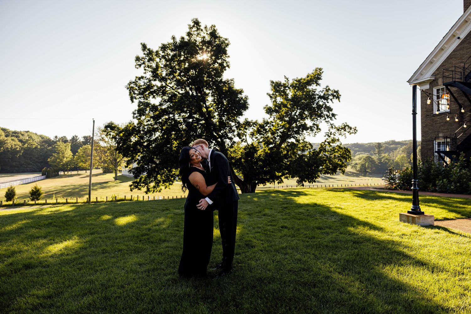 Romantic outdoor engagement portrait of a couple embracing on the sunlit lawn at Felt Estate in Michigan.