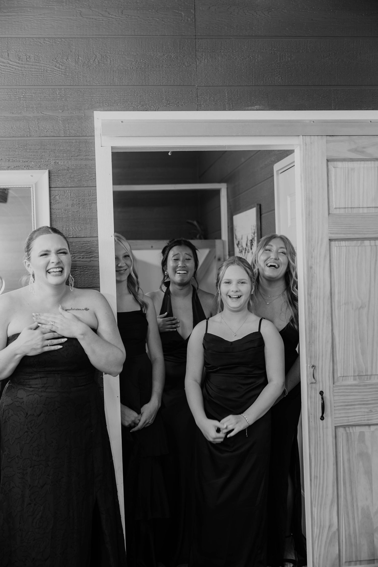 Black-and-white candid wedding photo of bridesmaids in matching dark dresses sharing an emotional moment at Res-Les Farms.