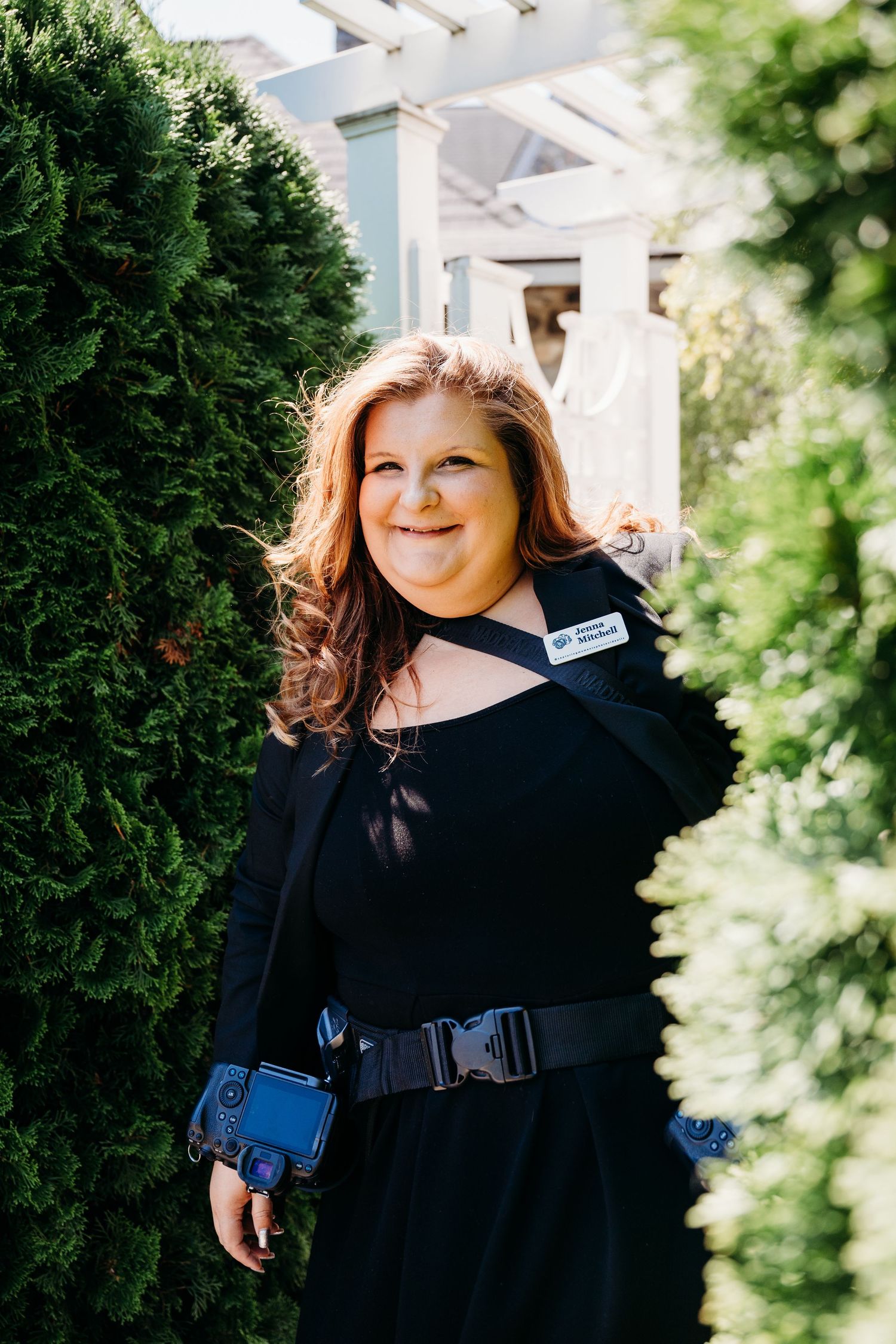 Outdoor portrait of a red-haired woman wearing a black dress beside lush greenery and stone architecture at Castle Farms, Michigan.