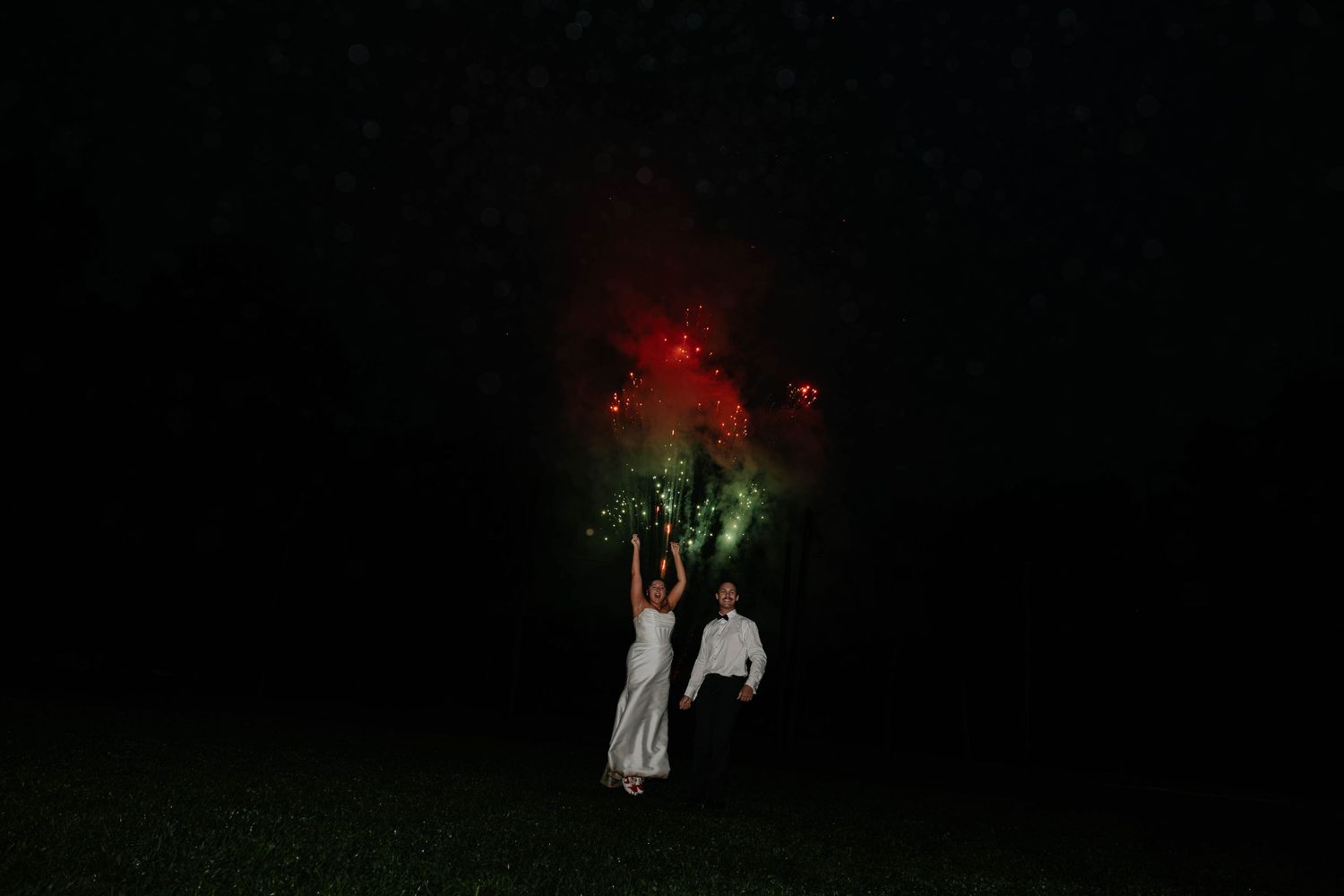 Bride and groom share a romantic nighttime wedding portrait beneath glowing fireworks in Battle Creek, Michigan.
