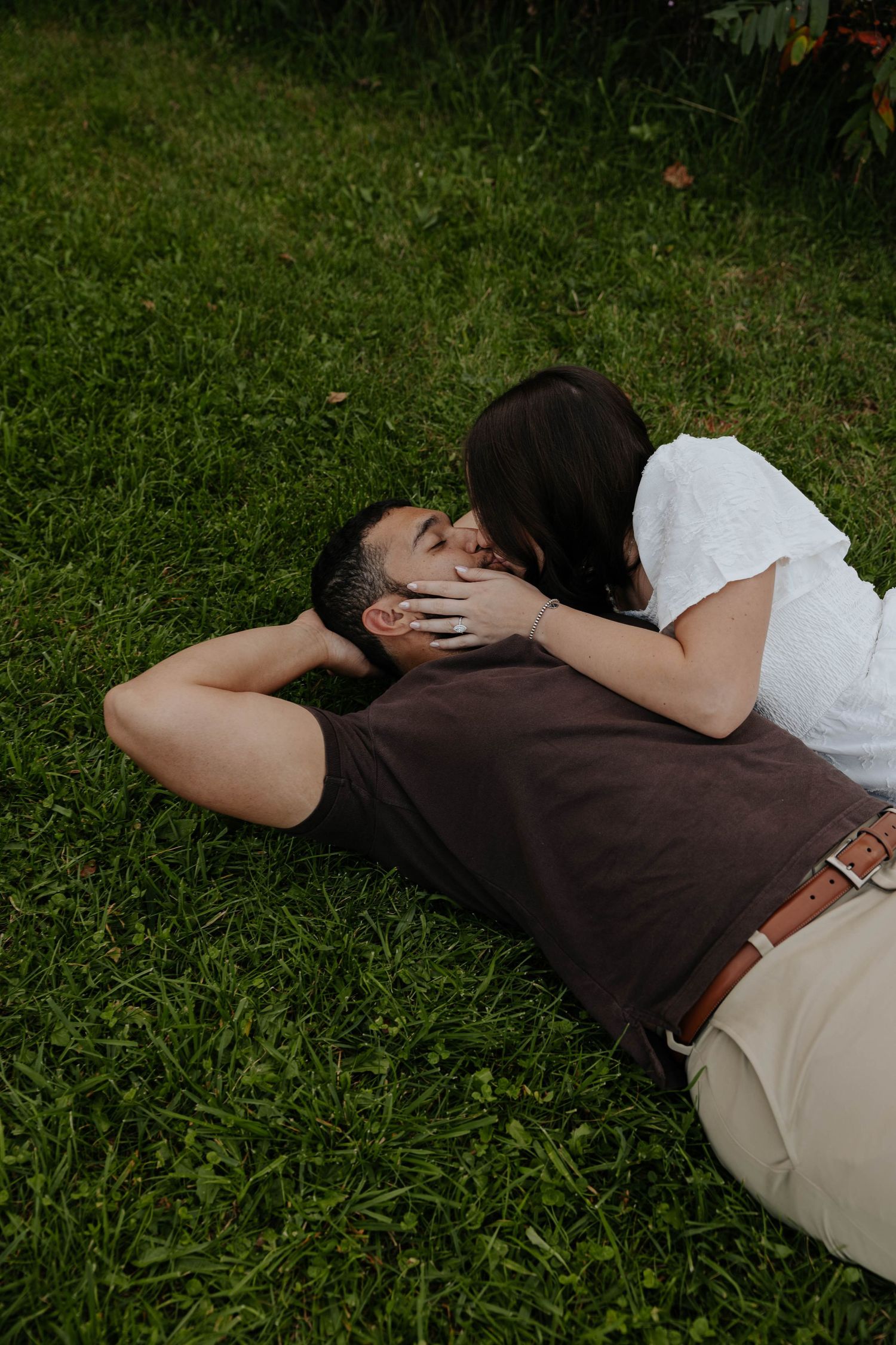 Candid engagement photo of a couple lying together in the grass and embracing during an outdoor couples session in Caledonia, Michigan.