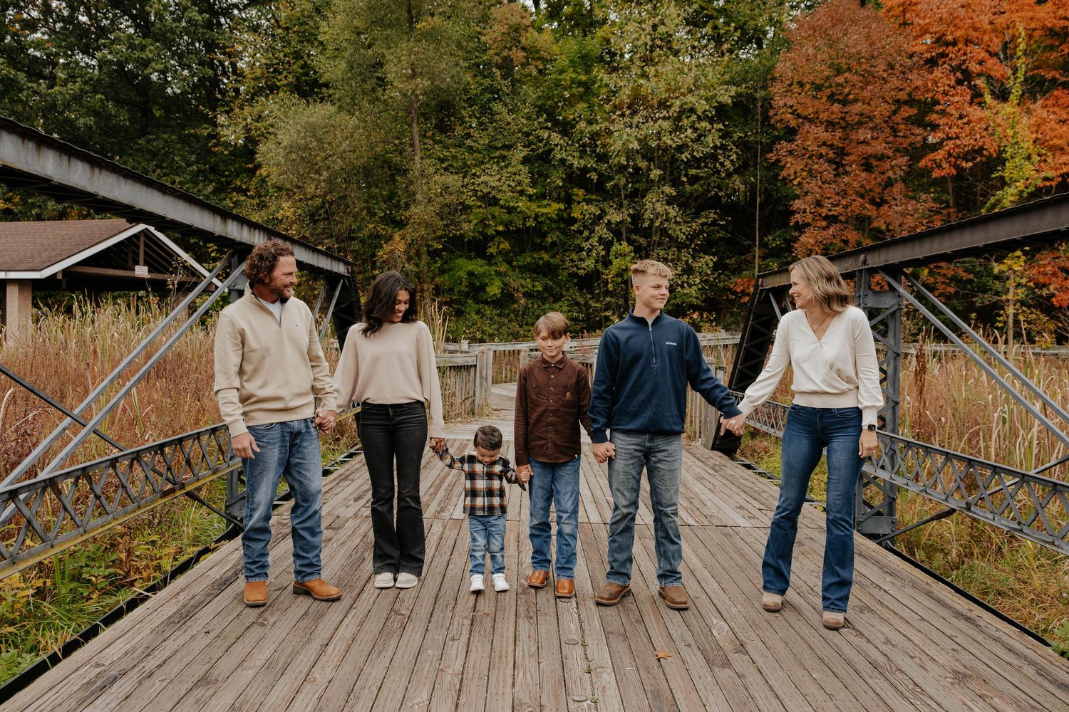 Fall family portraits on a rustic wooden bridge surrounded by colorful autumn trees in Battle Creek, Michigan.
