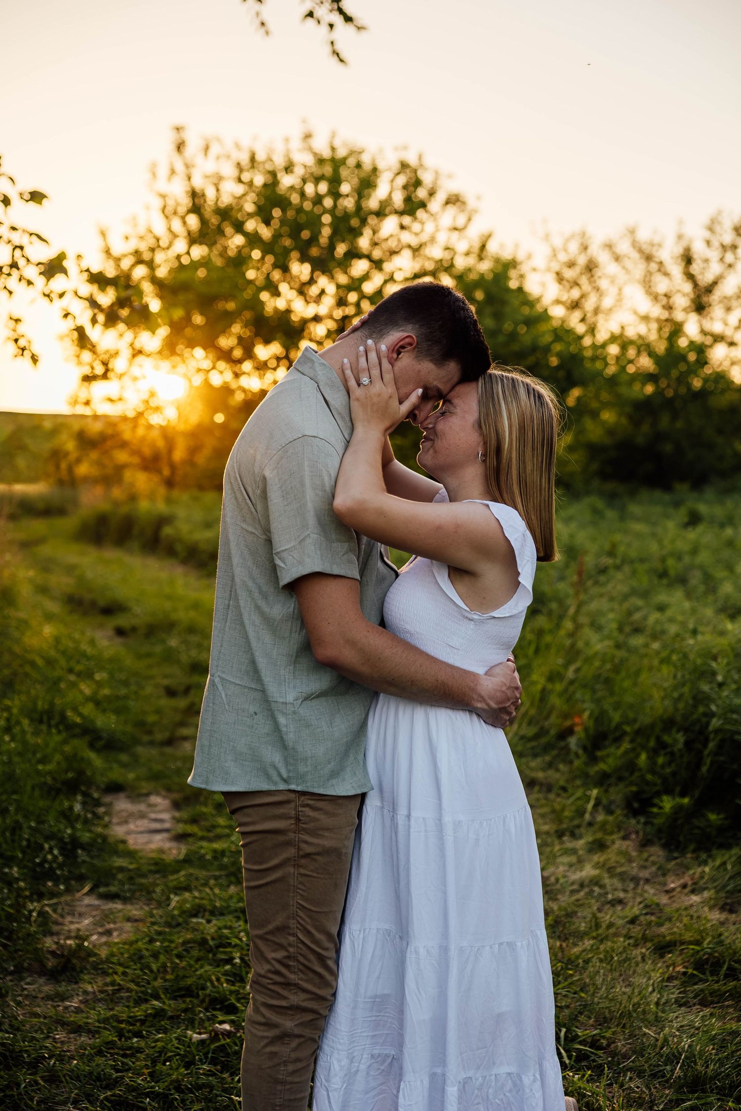 Golden hour engagement photo of a couple sharing a romantic embrace in a grassy field at sunset.