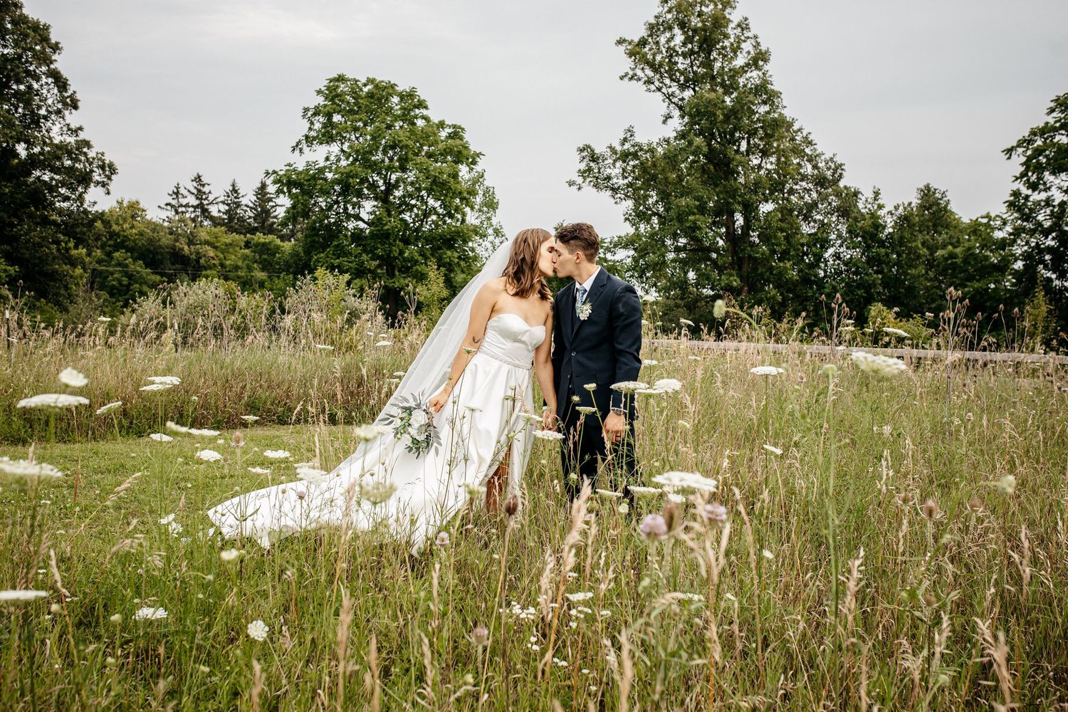 Bride and groom holding hands in a wildflower meadow, surrounded by soft greenery during their Michigan wedding portraits.