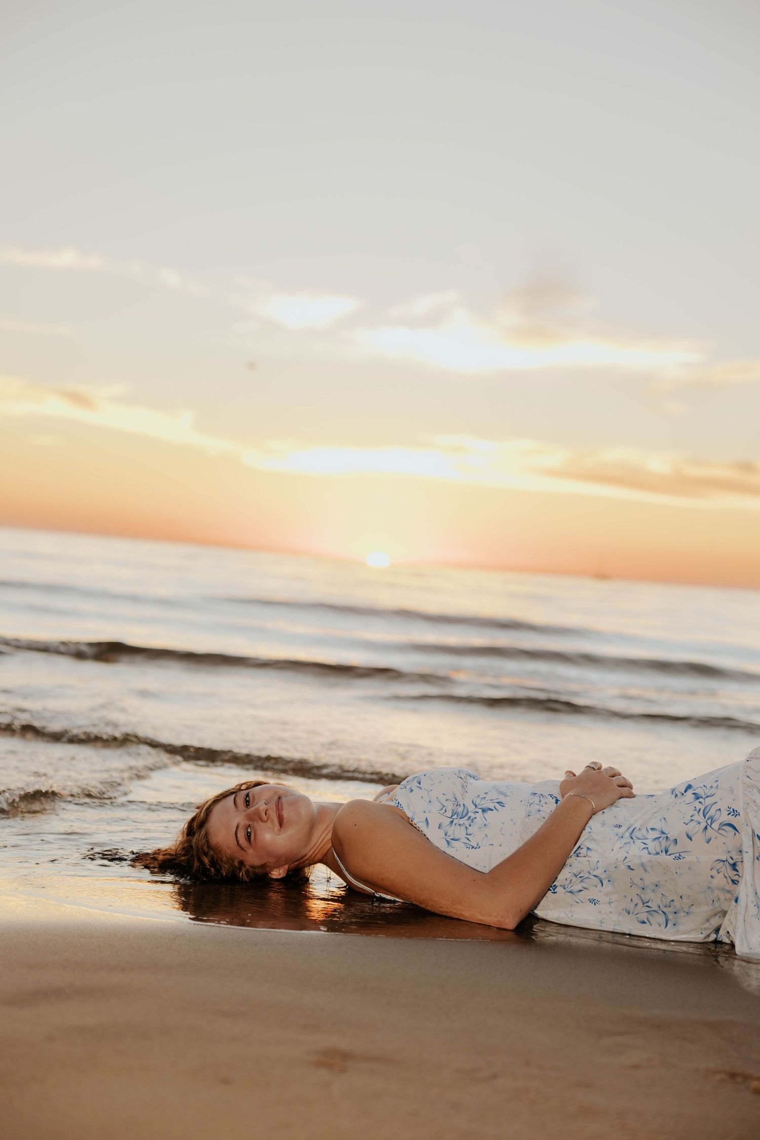 Beach senior portrait of a young woman relaxing on the sandy shoreline of Lake Michigan as gentle waves roll in during a golden sunset.