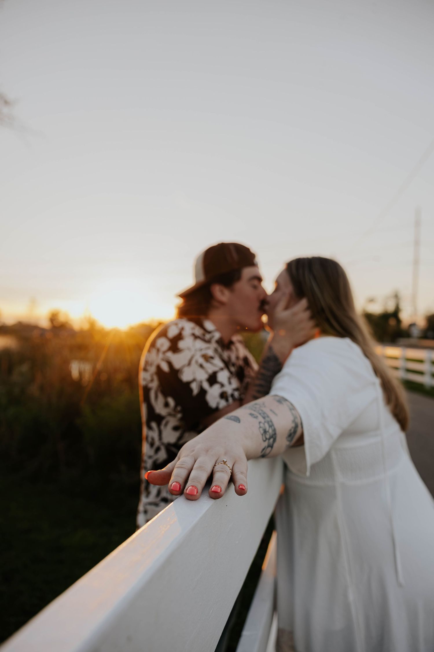 Romantic Celery Flats engagement photo of a couple kissing beside a white fence at sunset in Portage, Michigan.