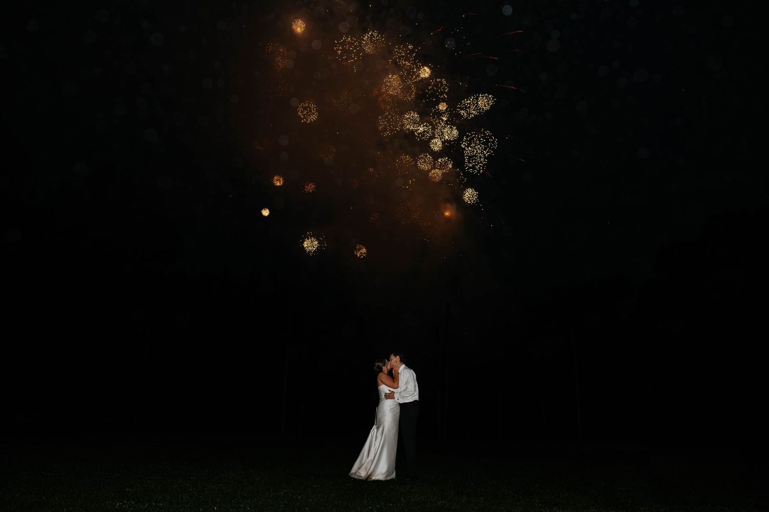 Bride and groom share a romantic nighttime wedding portrait beneath glowing fireworks in Battle Creek, Michigan.