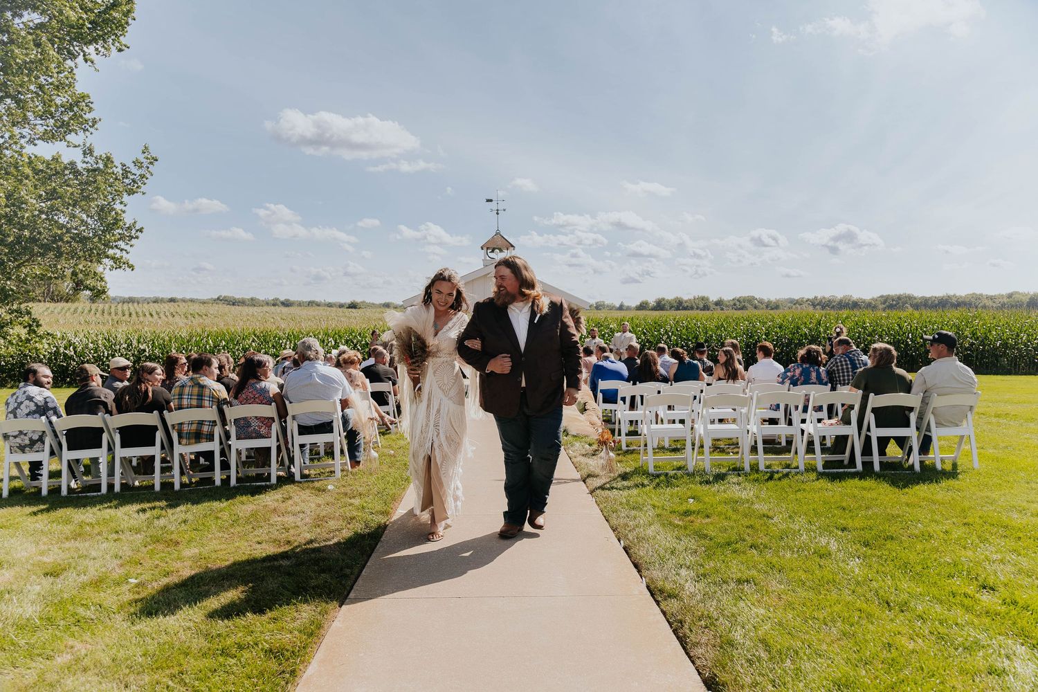 Bride walks down the aisle with her father during an outdoor wedding ceremony at The Gather in Allegan, Michigan.
