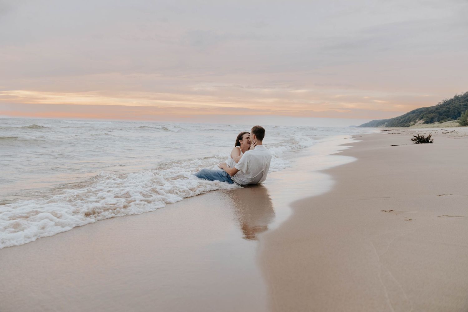 Romantic Holland, Michigan beach engagement photo of a couple embracing at the water's edge during a Lake Michigan sunset.