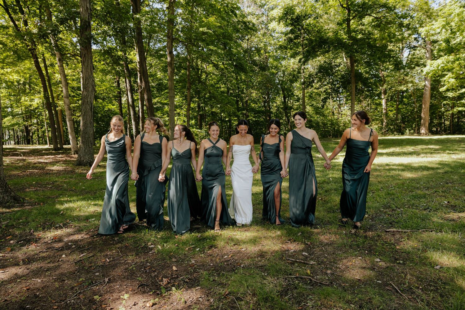 Bride and wedding party posing together beneath the trees at Hidden Oak Manor in Indiana, surrounded by lush summer greenery.