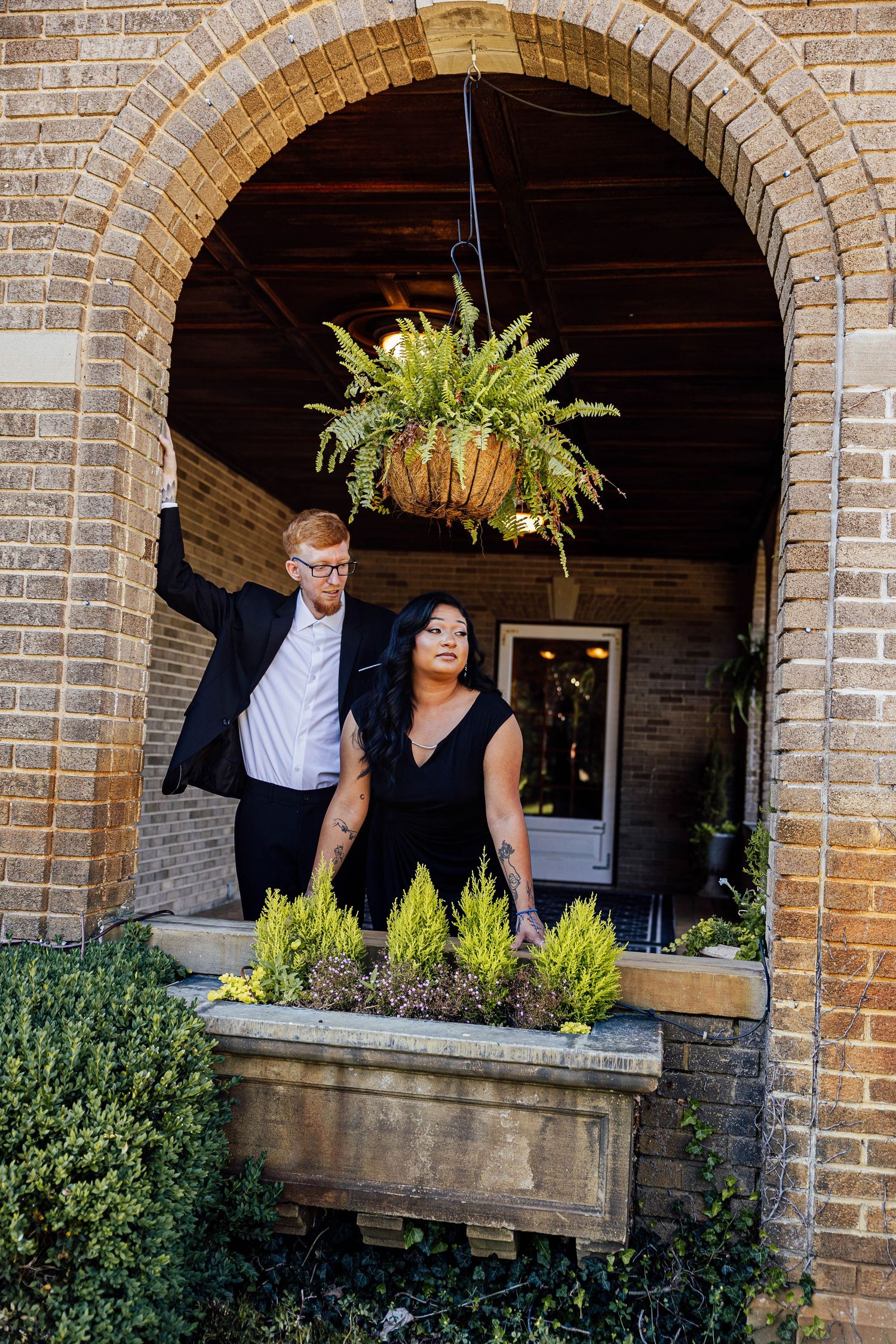 Editorial engagement photo of a couple posing together beneath a stone archway at Felt Estate, surrounded by greenery.