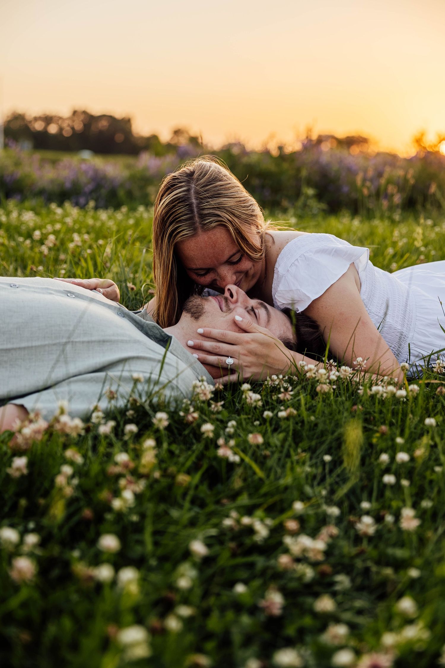 Romantic engagement photo of a couple lying together in a field of wildflowers at sunset near Kalamazoo, Michigan.